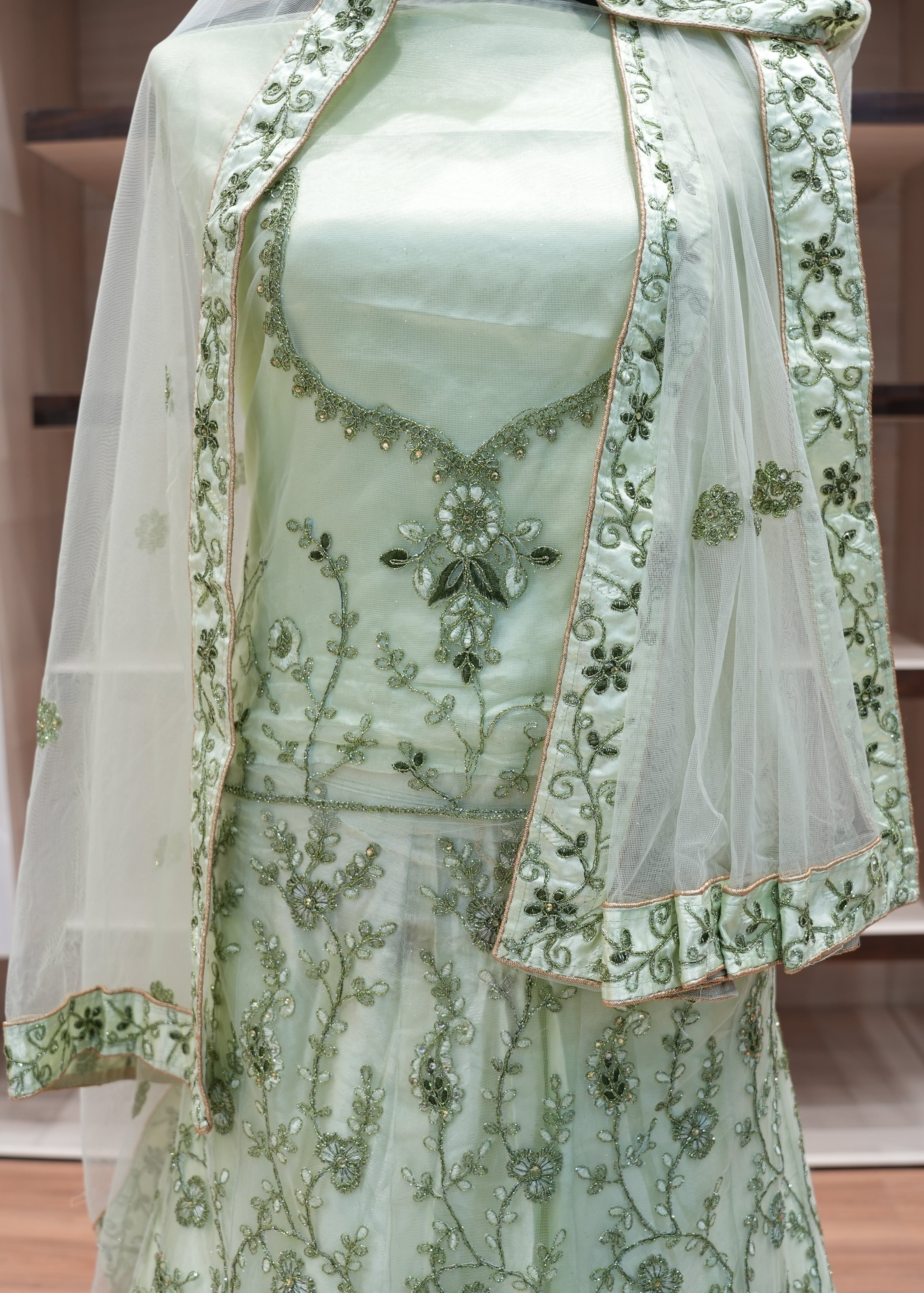 Light green embroidered outfit with a sheer dupatta on a wooden floor.
