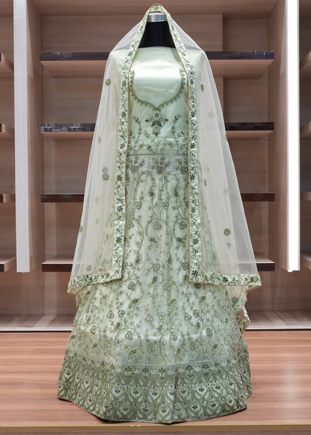 Green embroidered dress with a matching veil on a mannequin against a wooden background