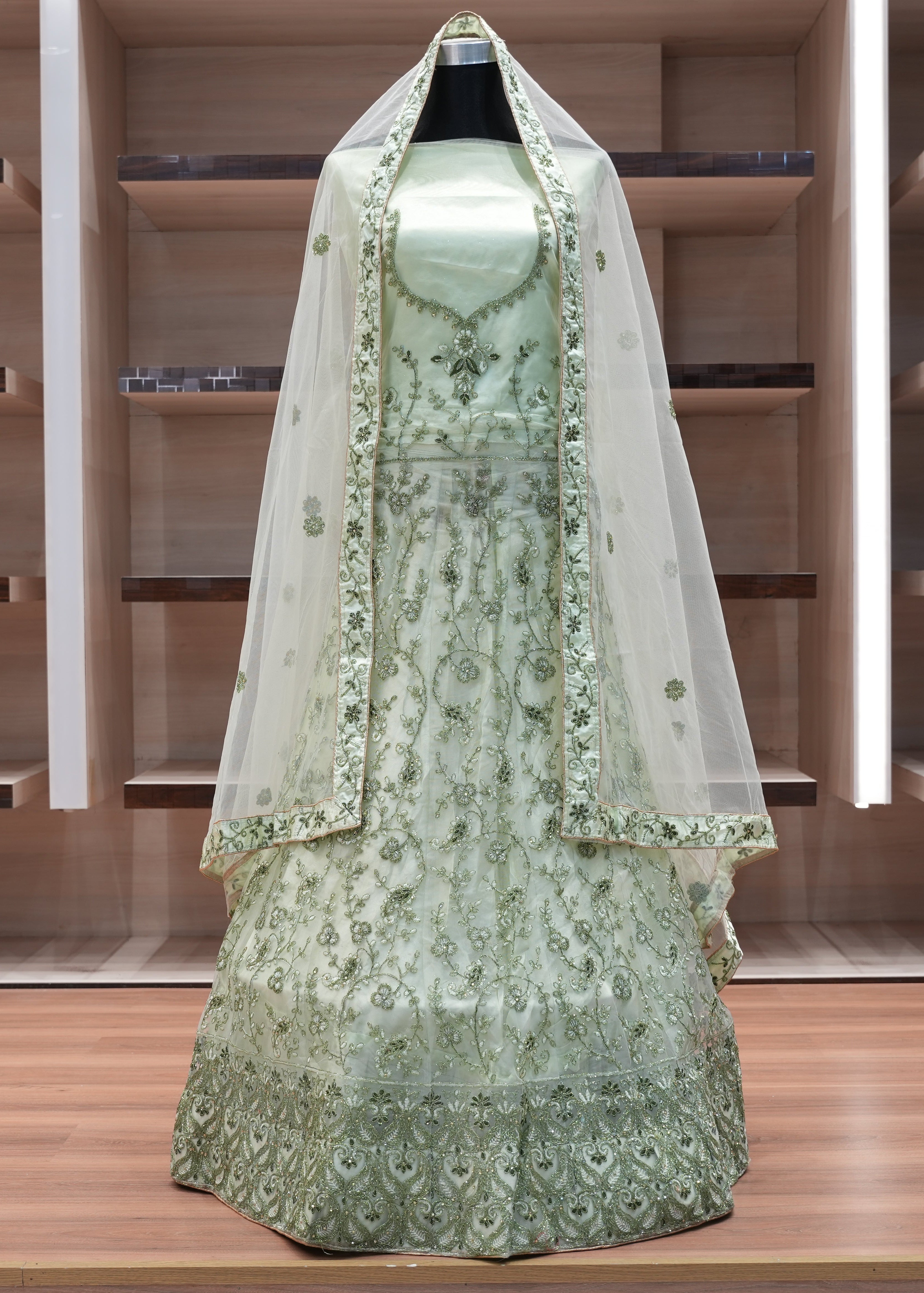 Green embroidered dress with a matching veil on a mannequin against a wooden background