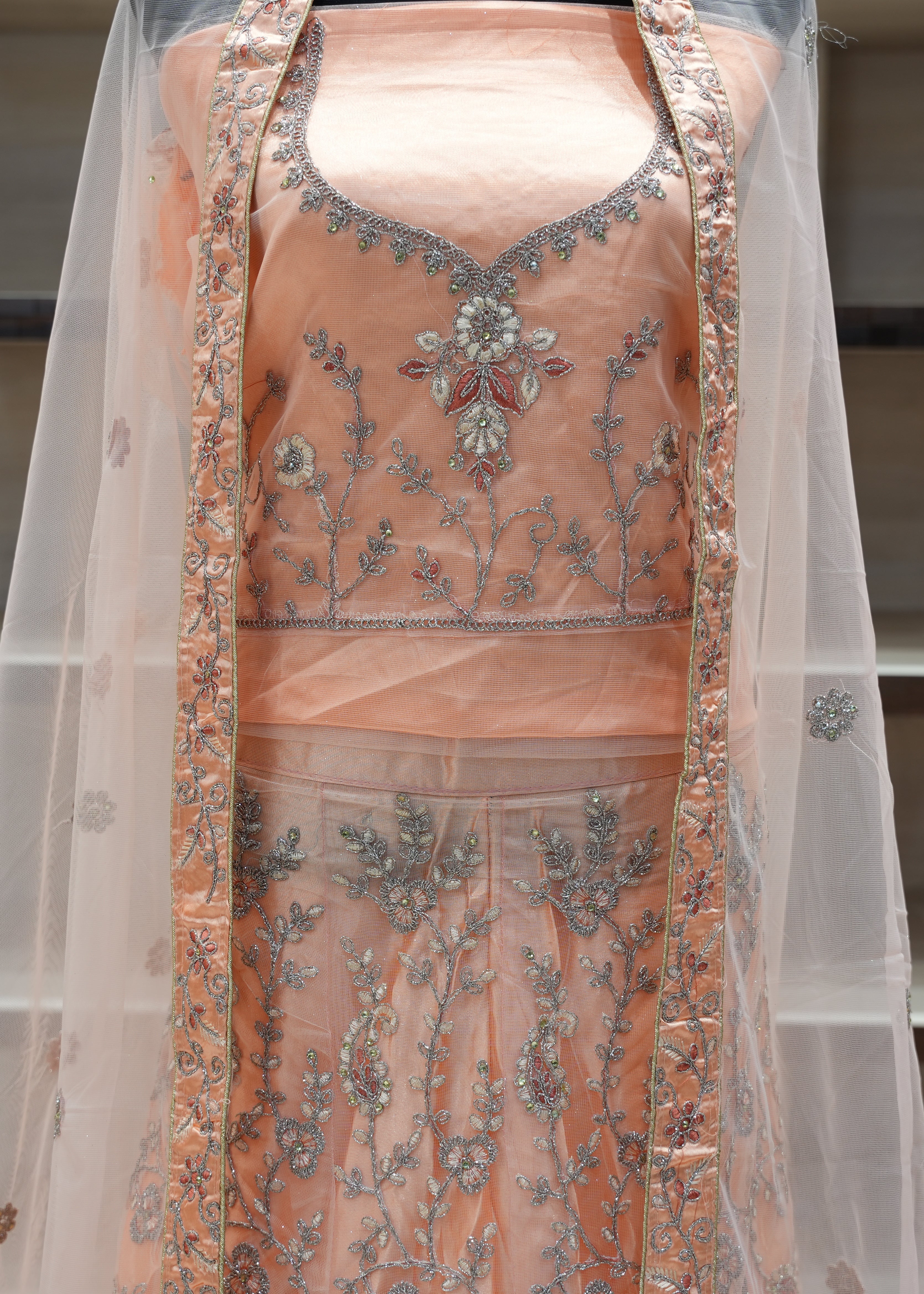 Peach-colored embroidered traditional outfit with a sheer dupatta on a neutral background