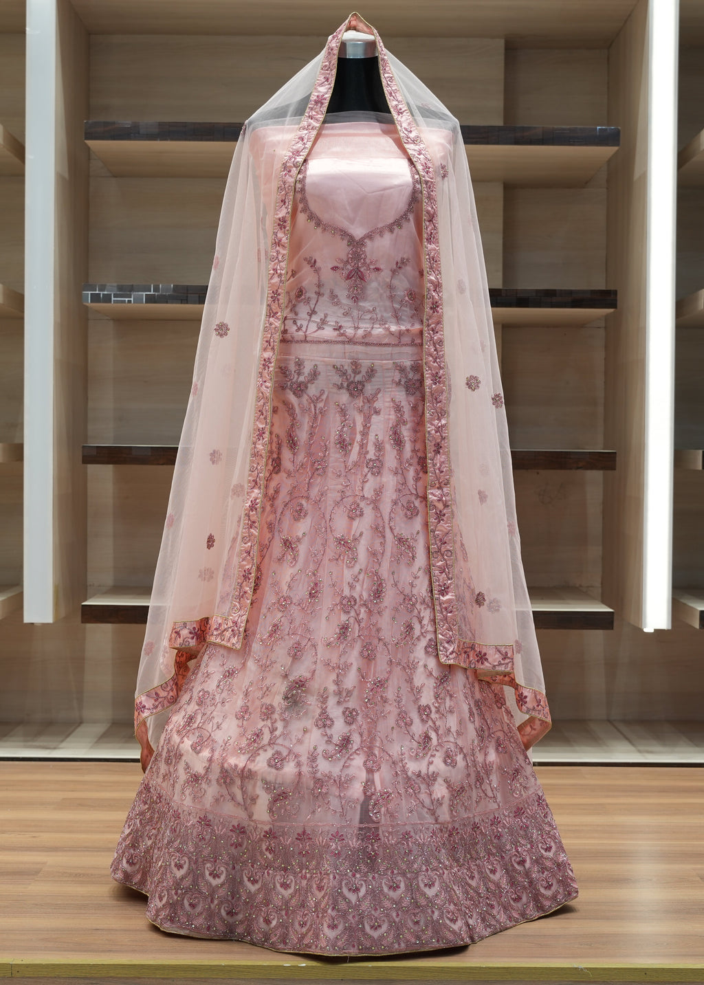 Pink embroidered dress with a veil on a mannequin against a wooden background