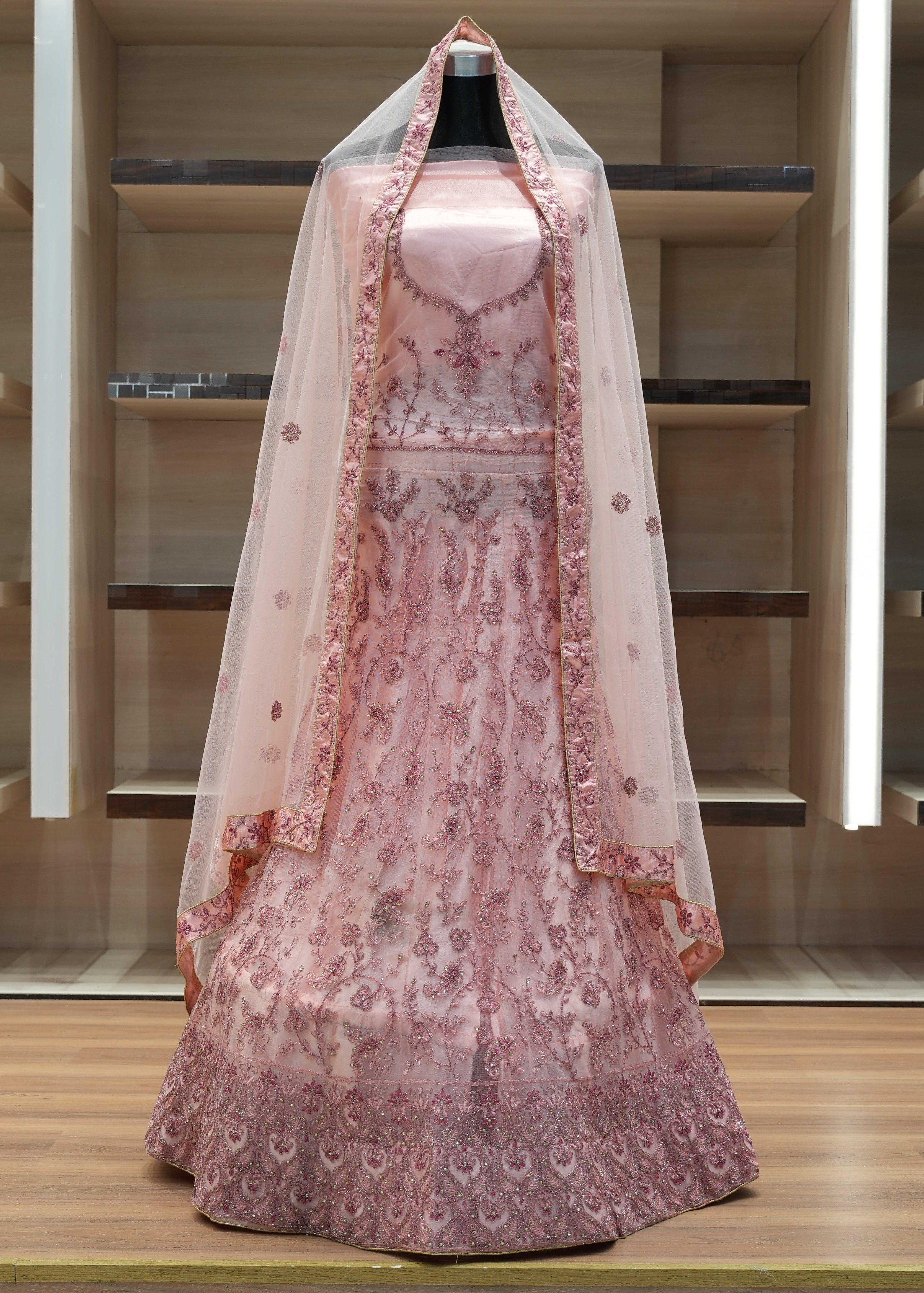 Pink embroidered dress with a veil on a mannequin against a wooden background