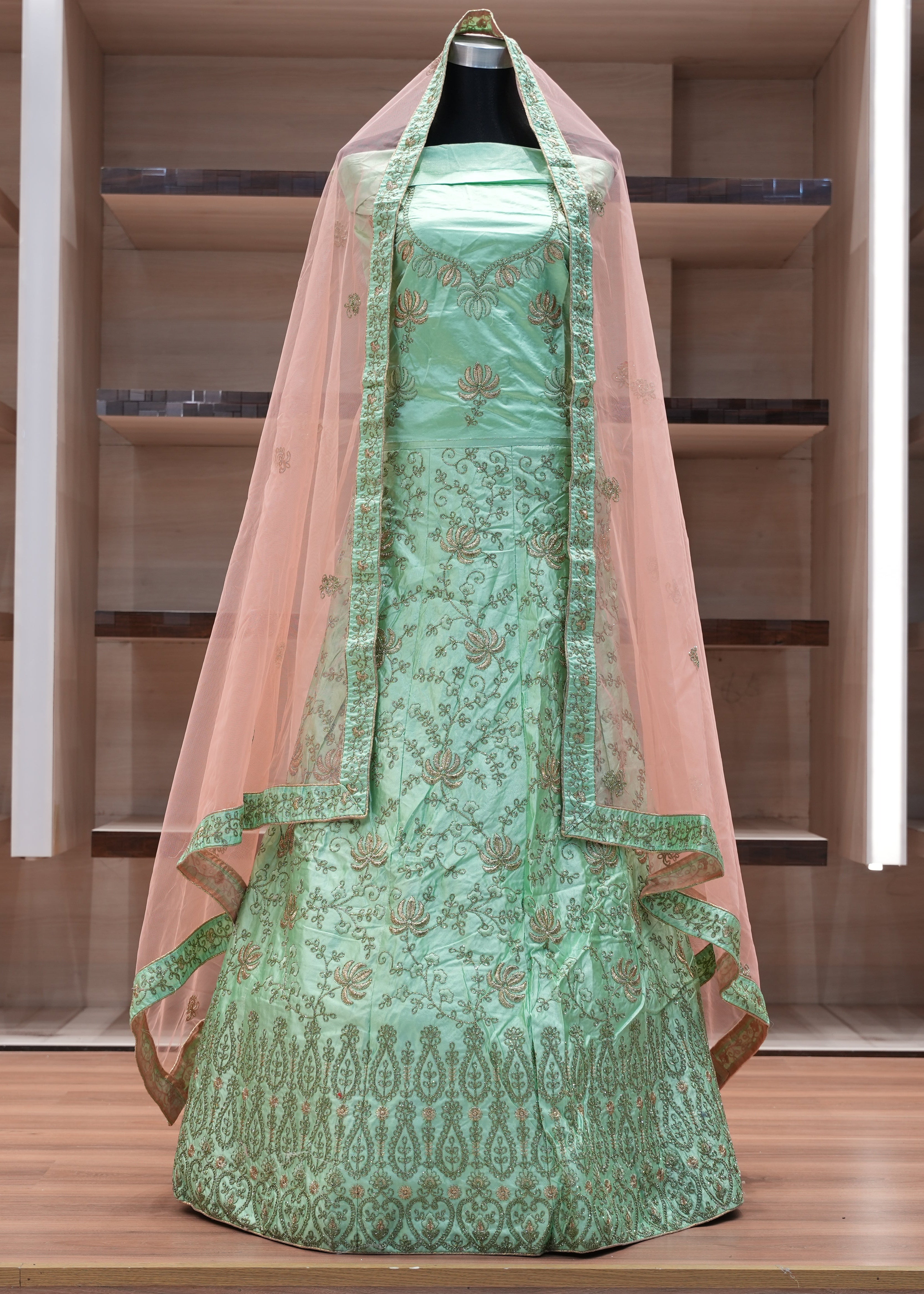 Green embroidered dress with a pink dupatta on a wooden shelf