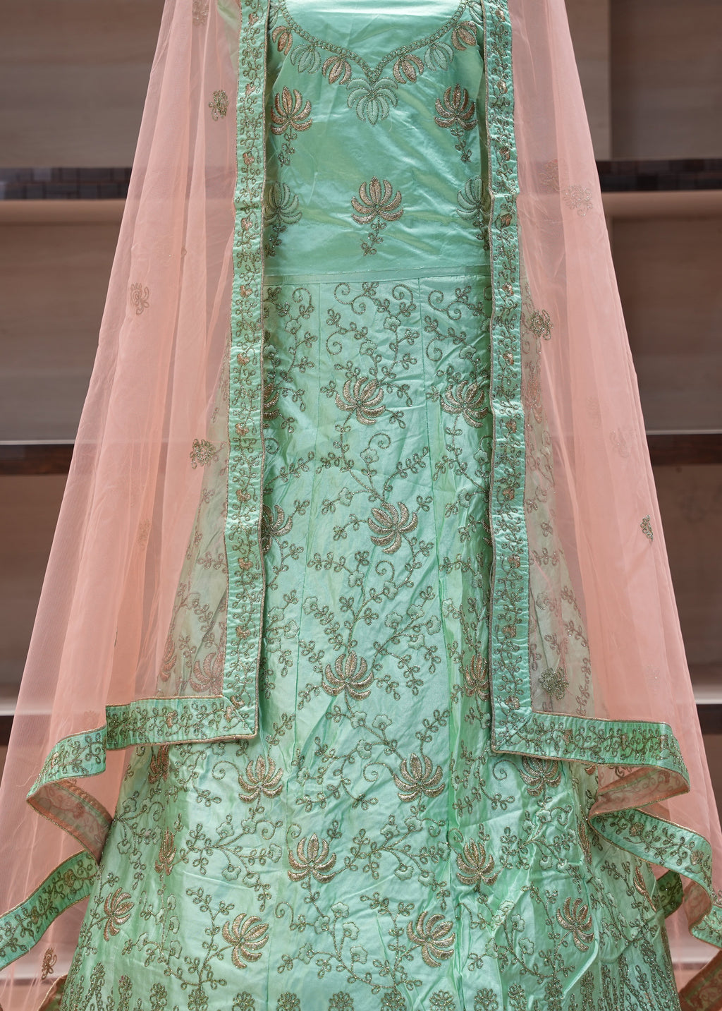 Green embroidered traditional outfit with a pink dupatta on a neutral background