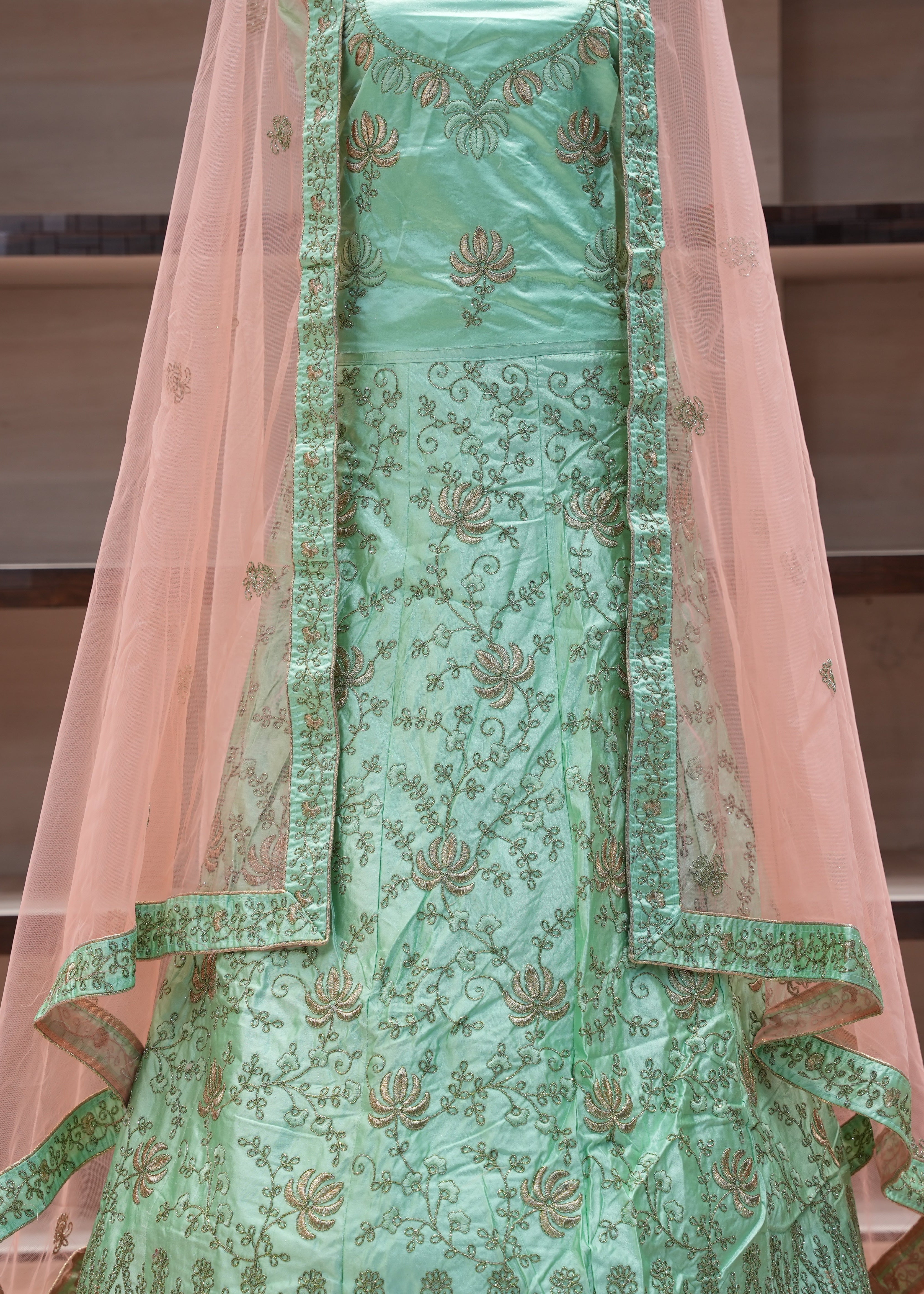 Green embroidered traditional outfit with a pink dupatta on a neutral background