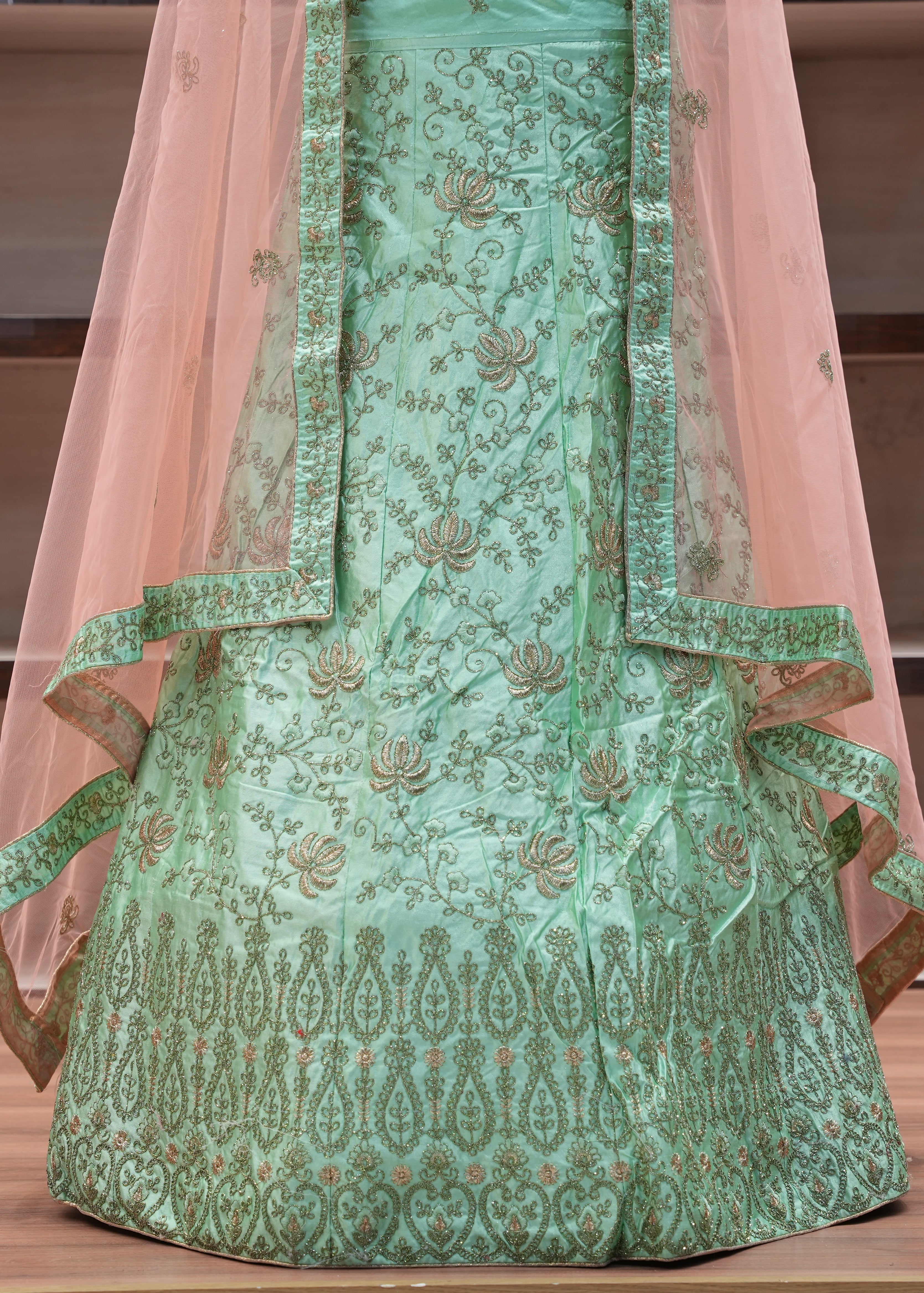 Green embroidered traditional outfit with pink dupatta on a wooden surface