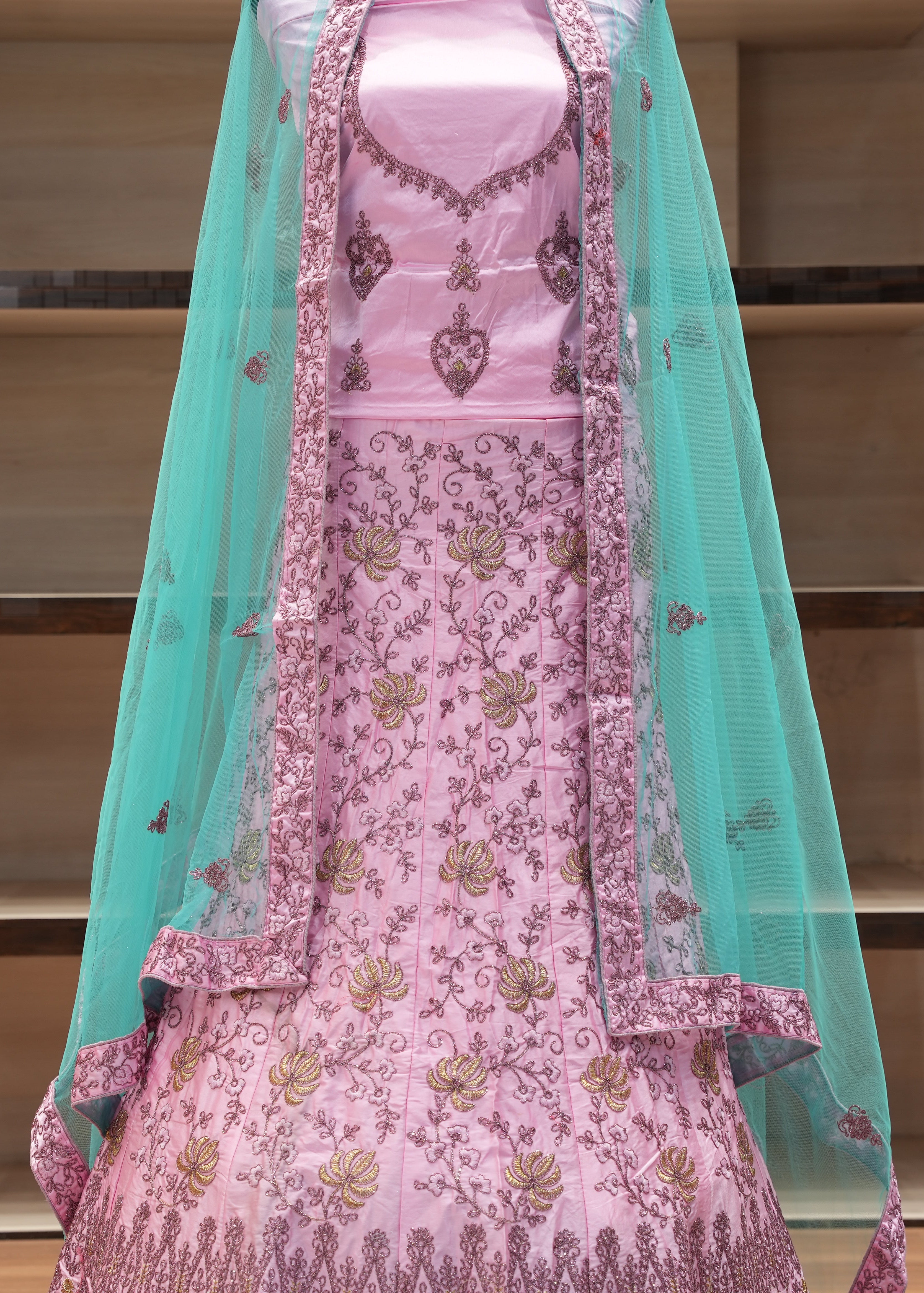 Pink embroidered traditional outfit with a turquoise dupatta on a mannequin against a neutral background.