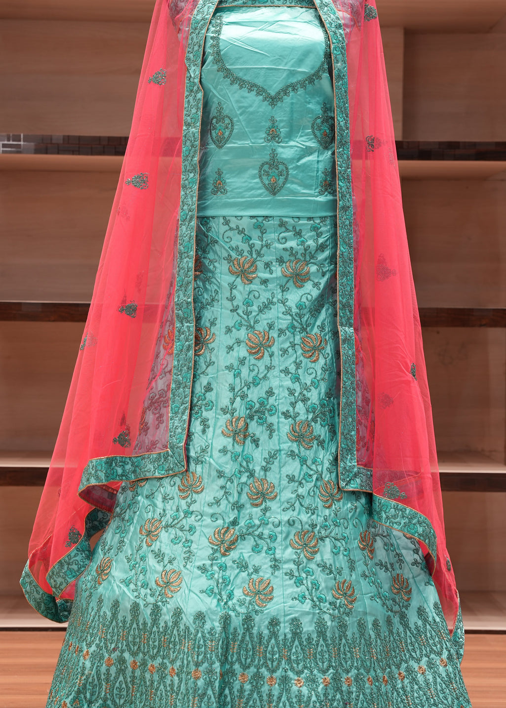 Traditional turquoise embroidered dress with a red dupatta on a wooden background