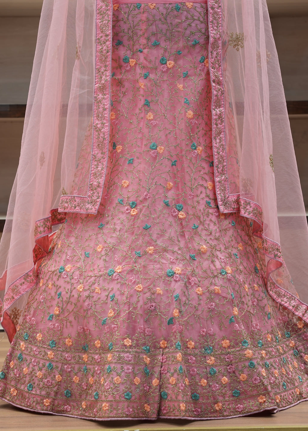 Pink embroidered traditional outfit with a sheer dupatta on a wooden surface.