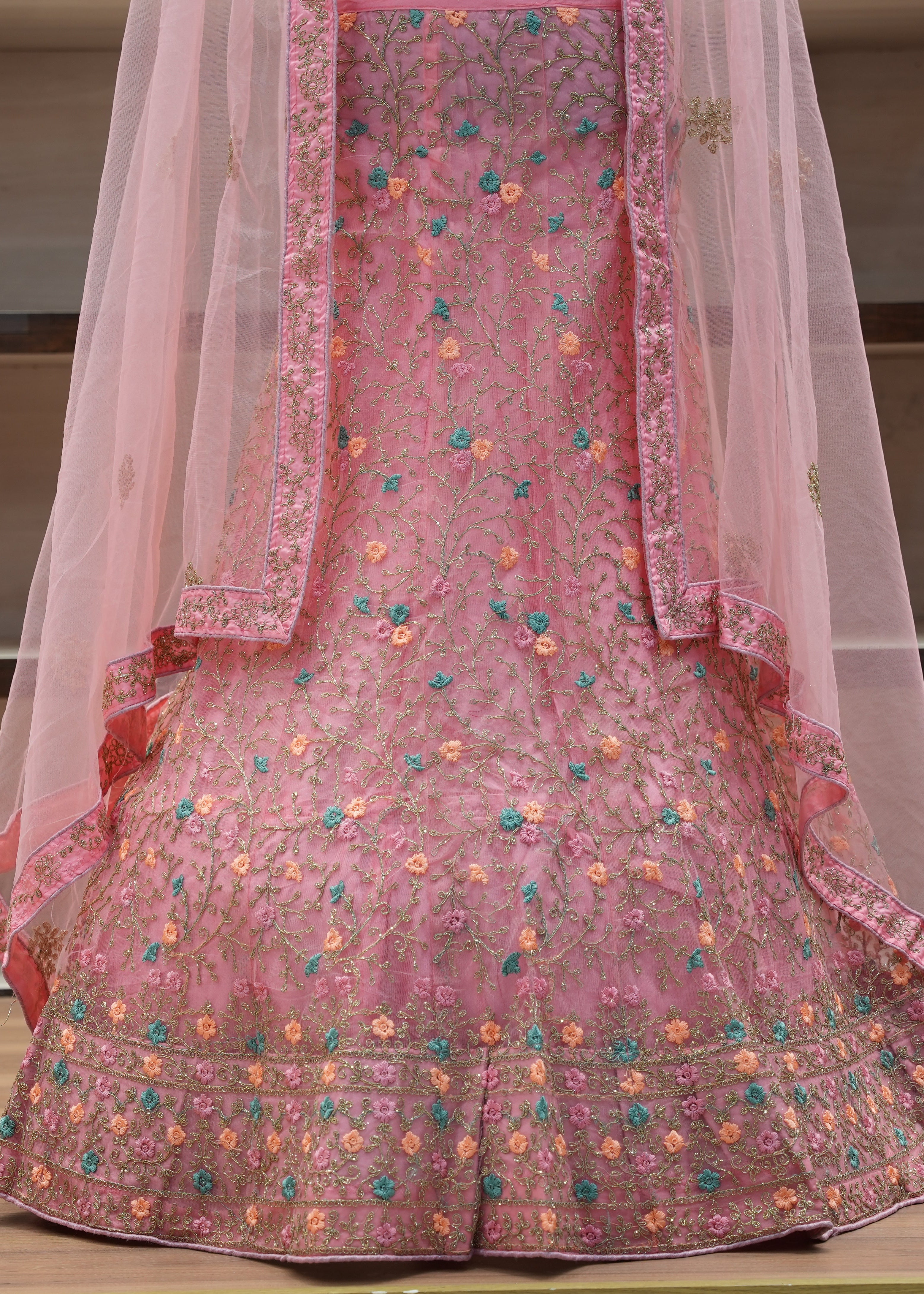 Pink embroidered traditional outfit with a sheer dupatta on a wooden surface.