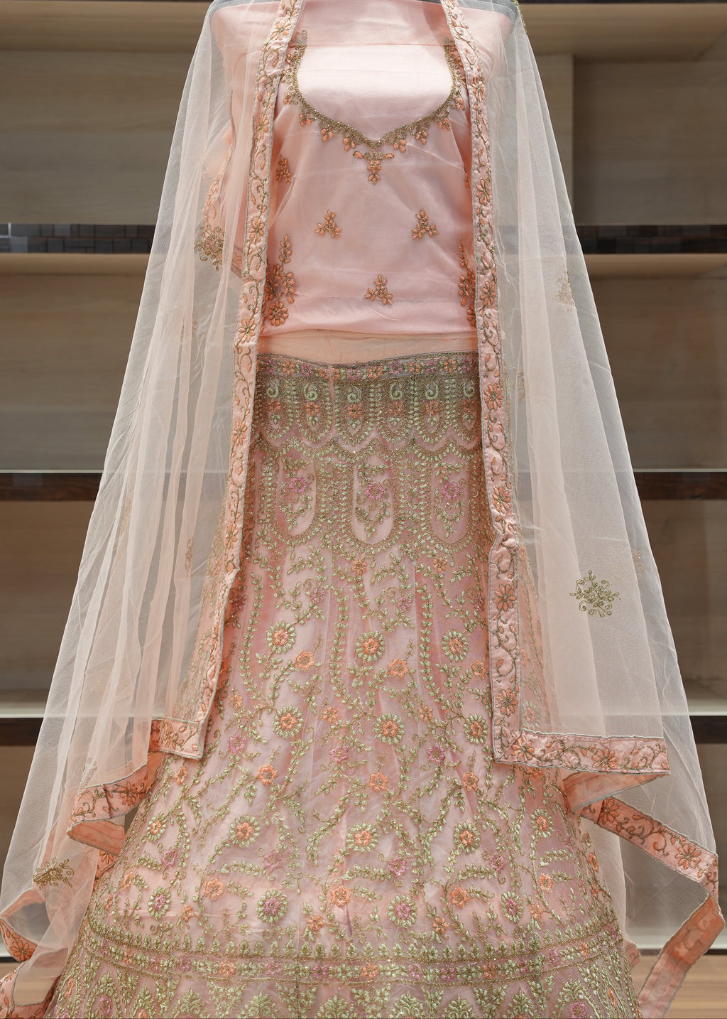 Traditional embroidered outfit with a pink blouse and green skirt on a mannequin, set against a neutral indoor background.