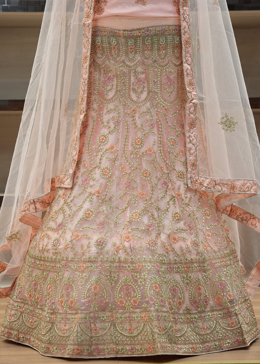 Traditional embroidered outfit with a sheer dupatta on a wooden surface