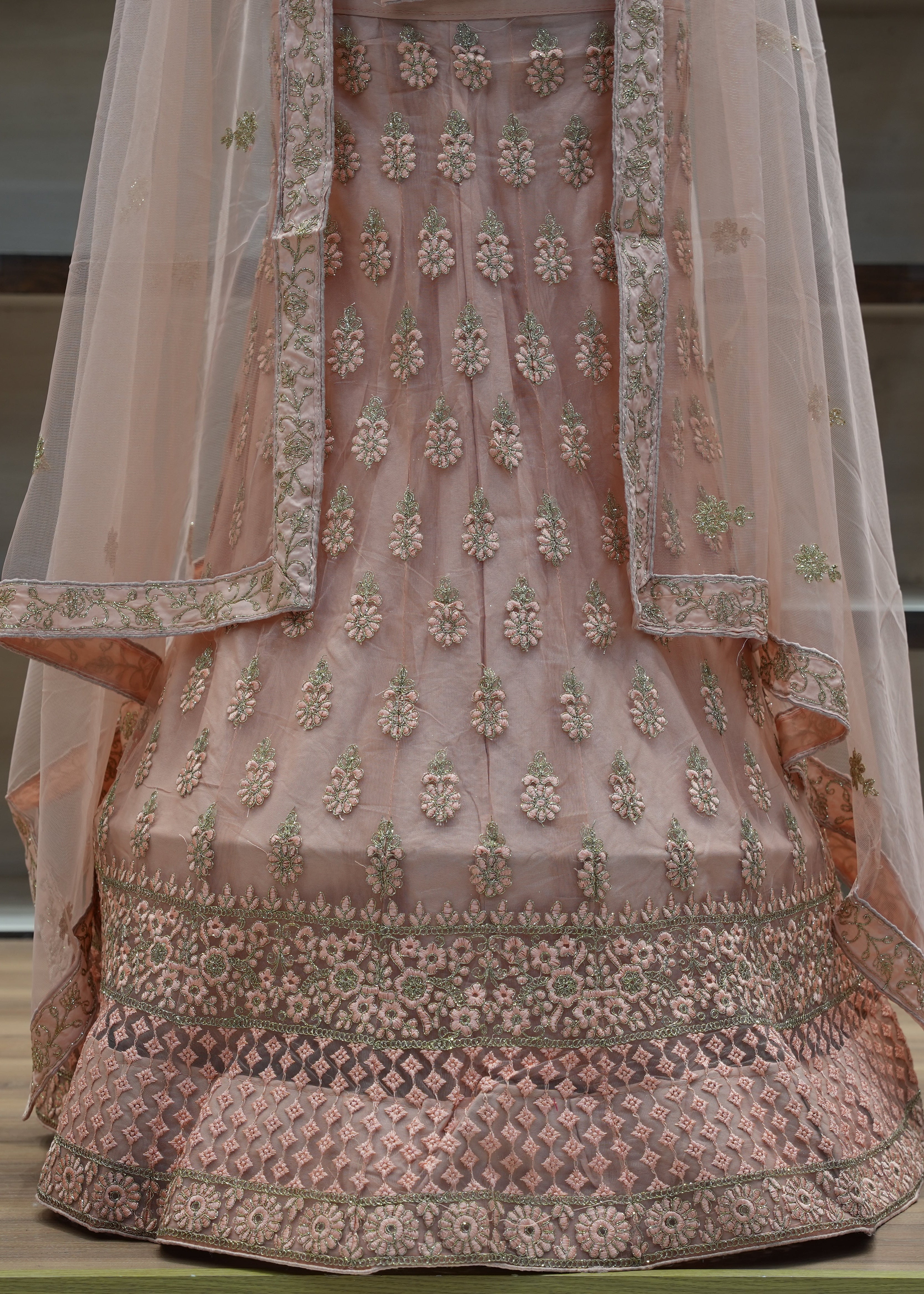 Traditional embroidered pink outfit with a sheer dupatta on a wooden surface.