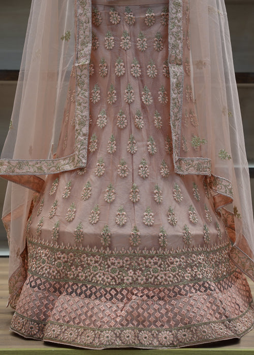 Traditional embroidered pink outfit with a sheer dupatta on a wooden surface.