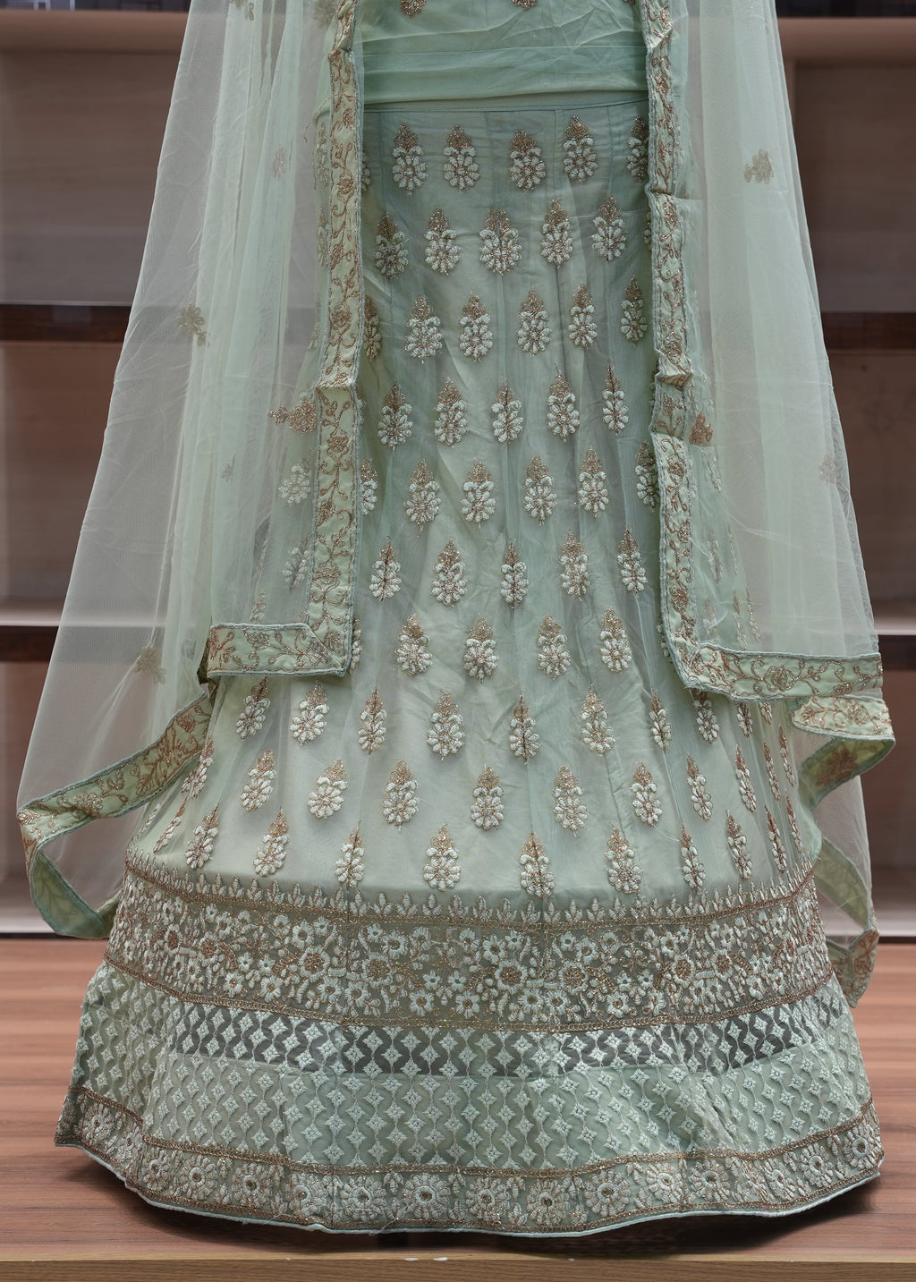 Light green embroidered traditional outfit with a sheer dupatta on a wooden surface.