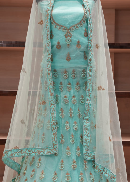 Turquoise embroidered dress with a sheer overlay on a wooden shelf background