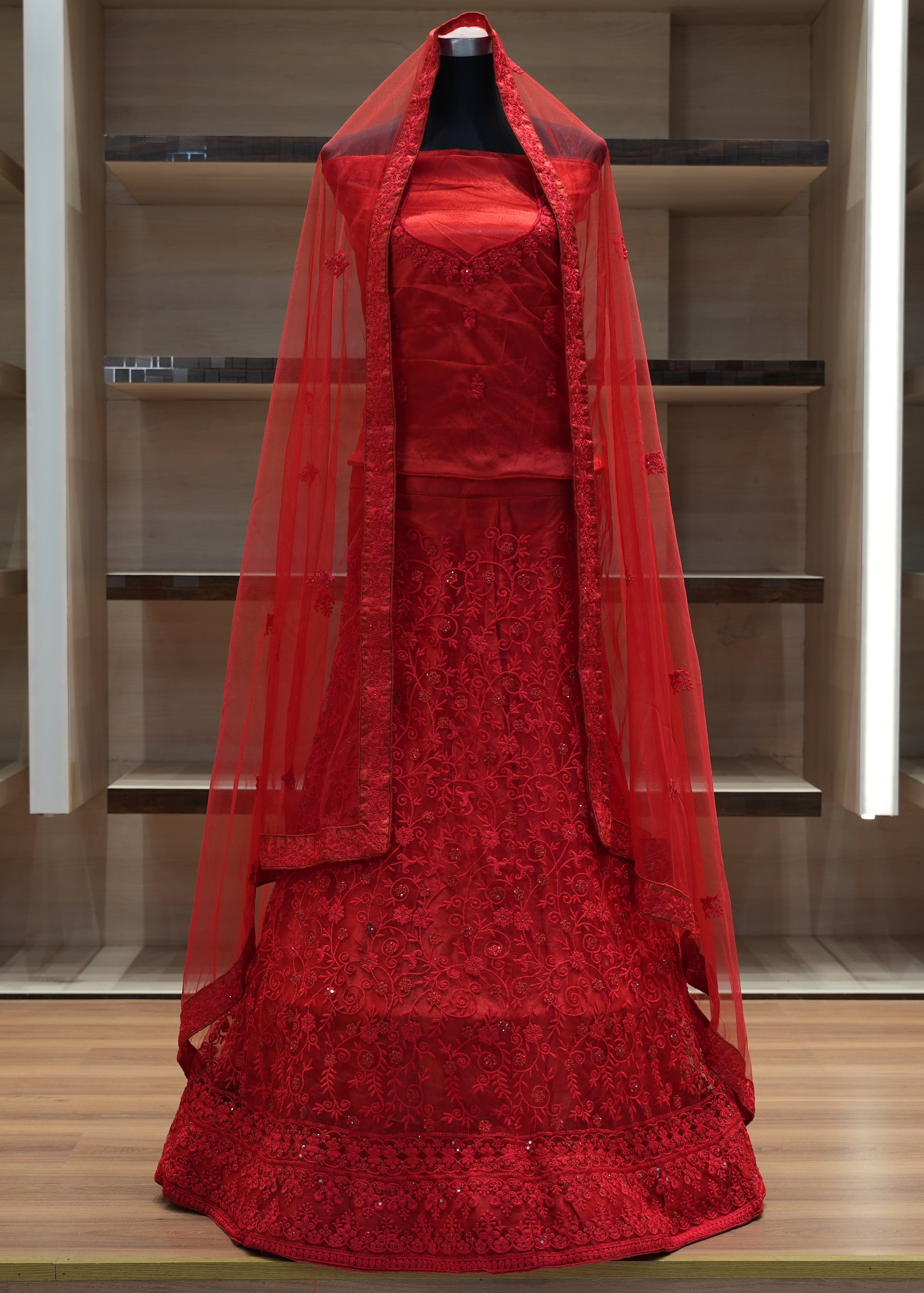 Red embroidered dress with a sheer overlay on a mannequin against a wooden panel background