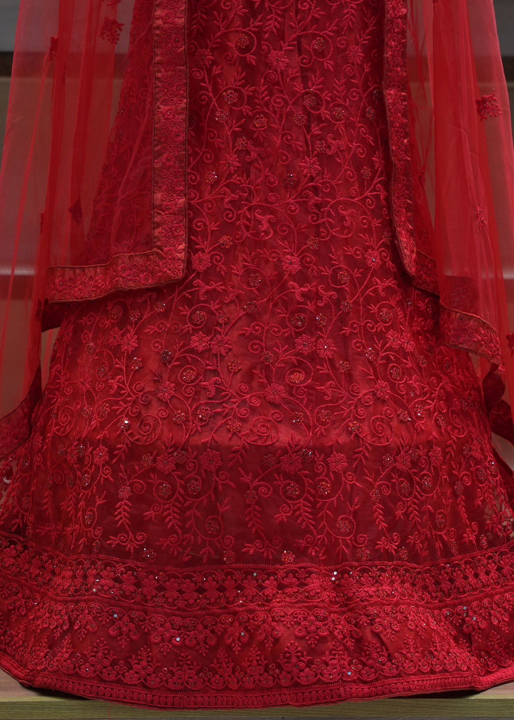 Red embroidered dress with a sheer overlay on a wooden floor.