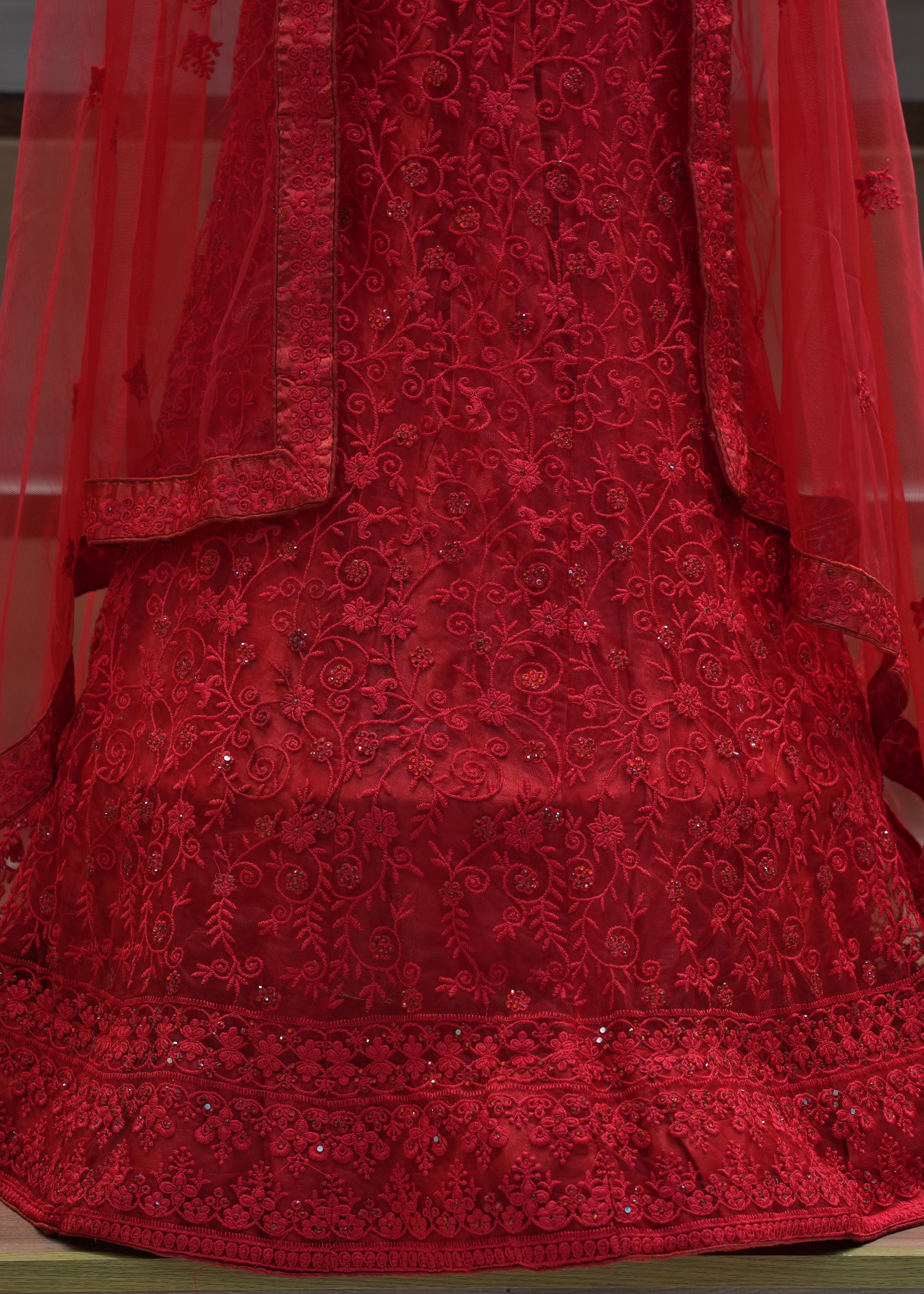 Red embroidered dress with a sheer overlay on a wooden floor.
