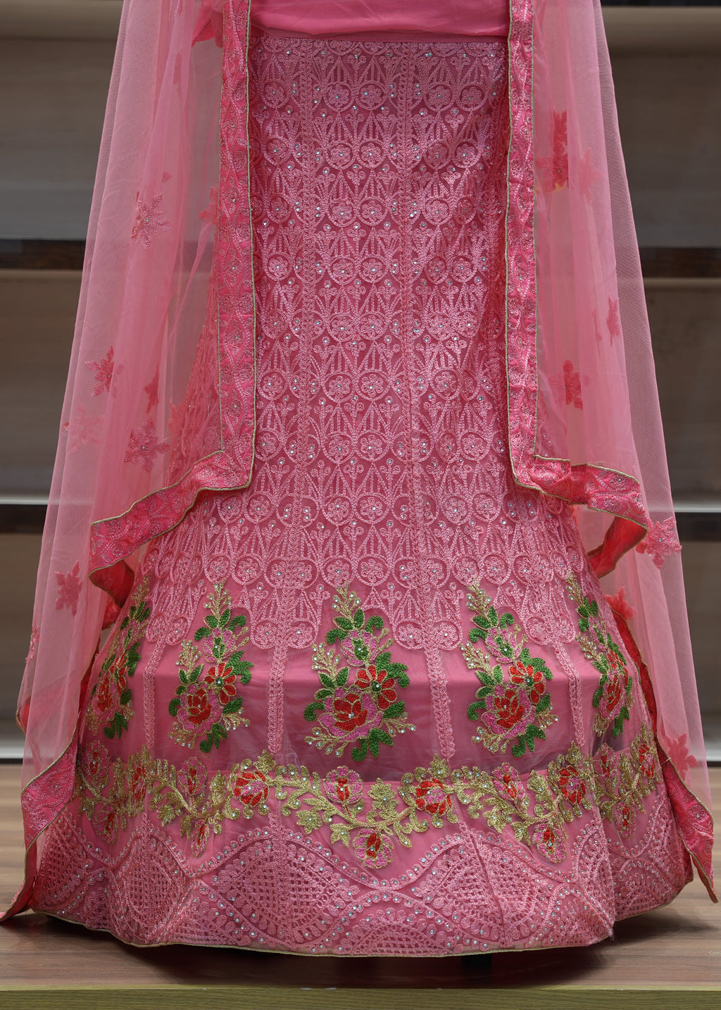 Pink embroidered traditional outfit with a sheer dupatta on a wooden surface.