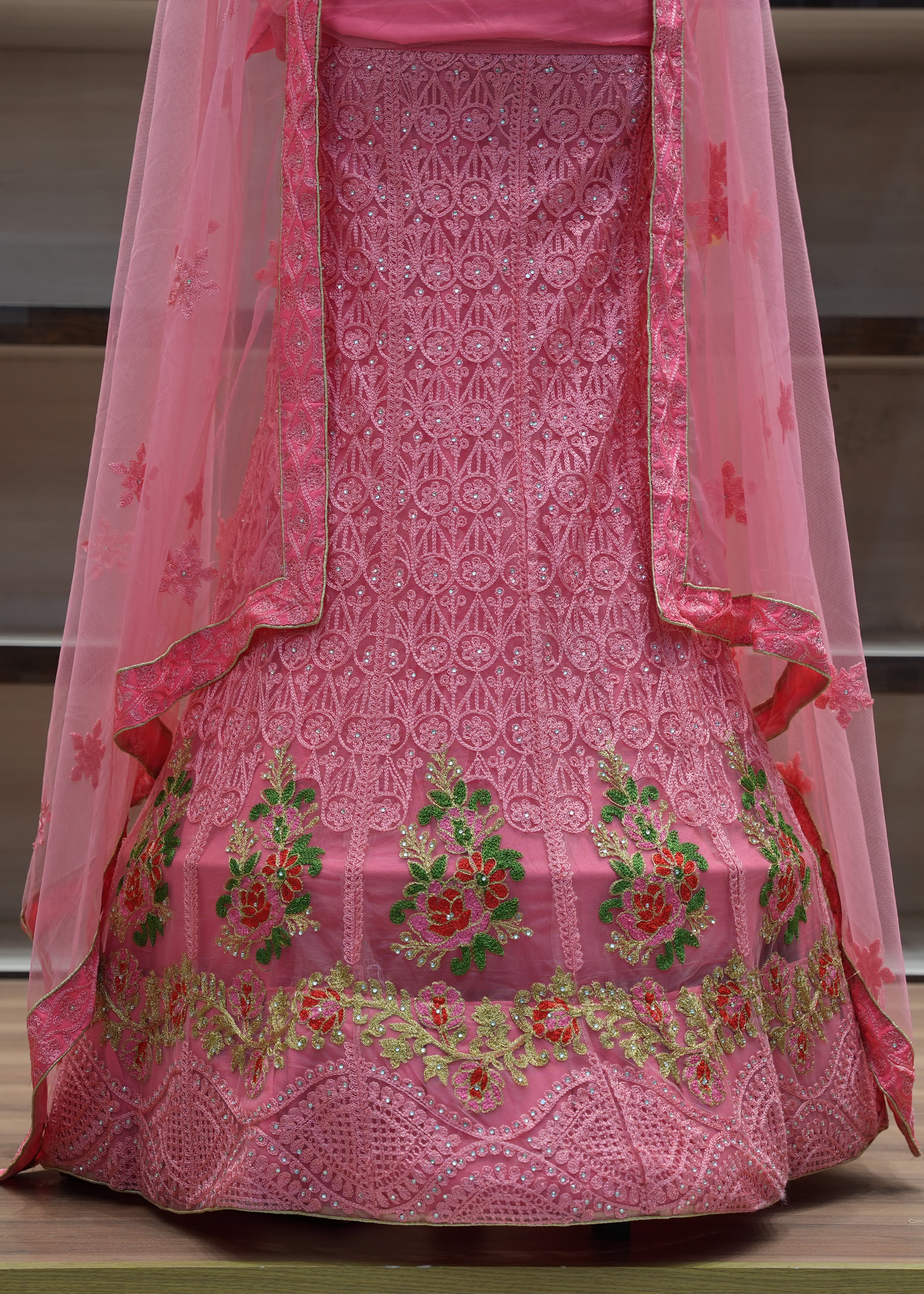 Pink embroidered traditional outfit with a sheer dupatta on a wooden surface.