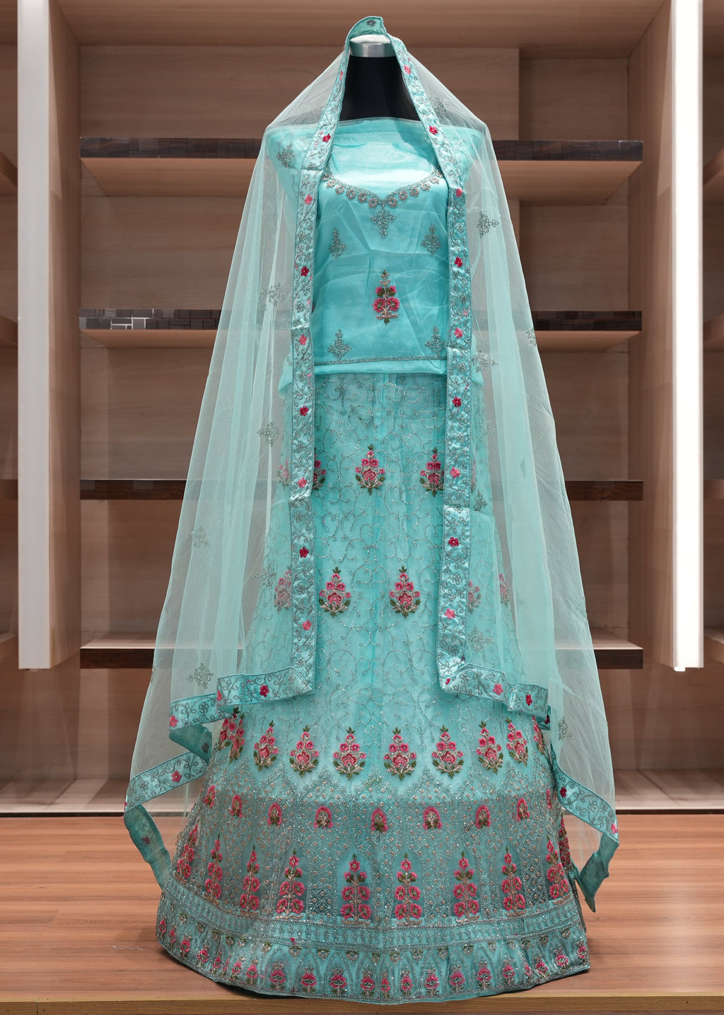 Turquoise embroidered traditional outfit with a sheer dupatta on a wooden shelf background