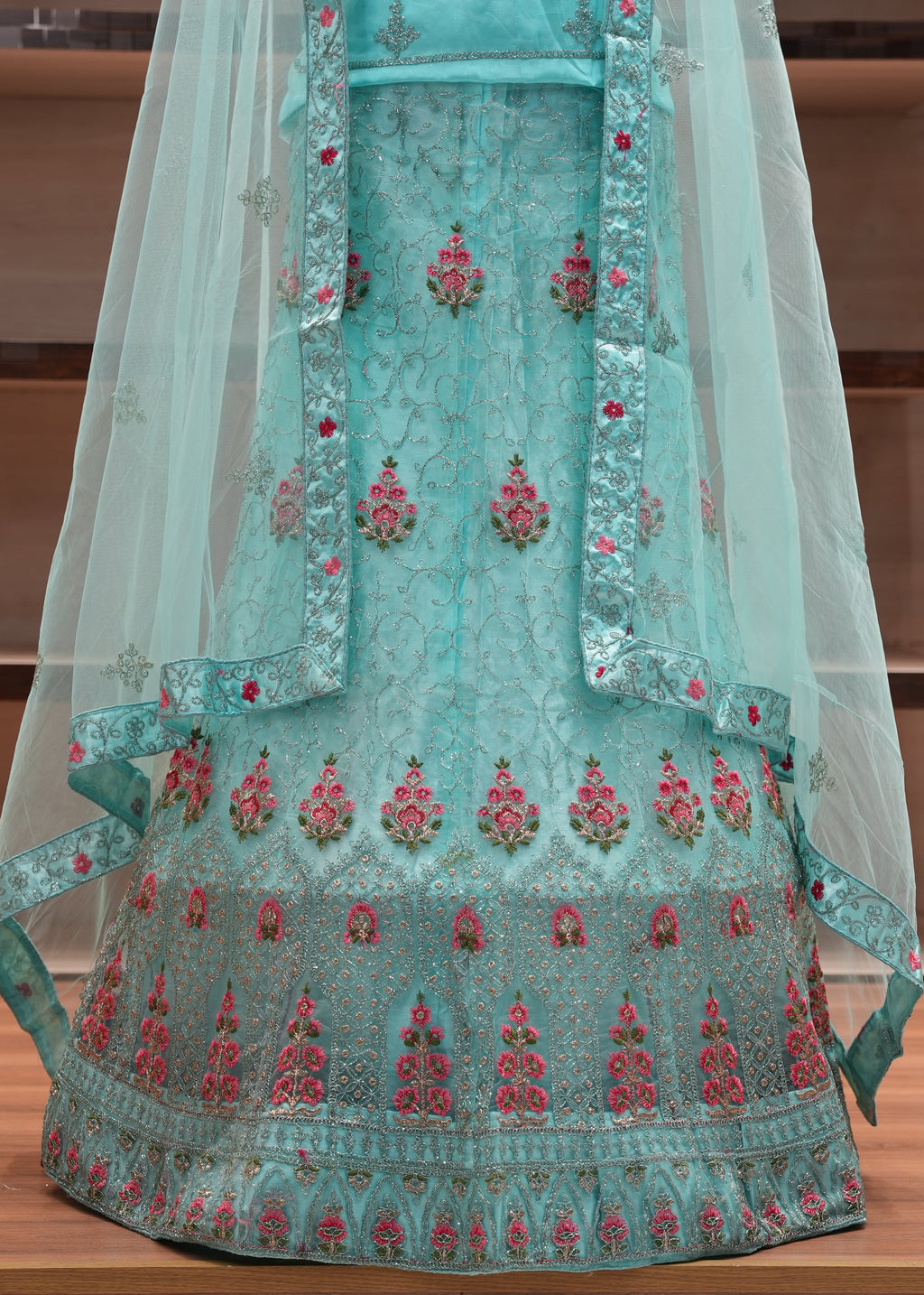Teal embroidered traditional outfit with a sheer dupatta on a wooden surface.