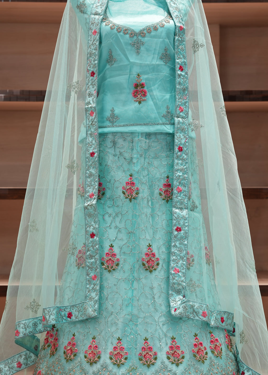 Turquoise embroidered traditional outfit with a sheer dupatta on a wooden shelf background