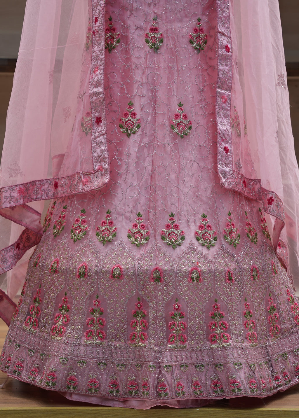 Pink embroidered traditional outfit with a sheer dupatta on a wooden surface.