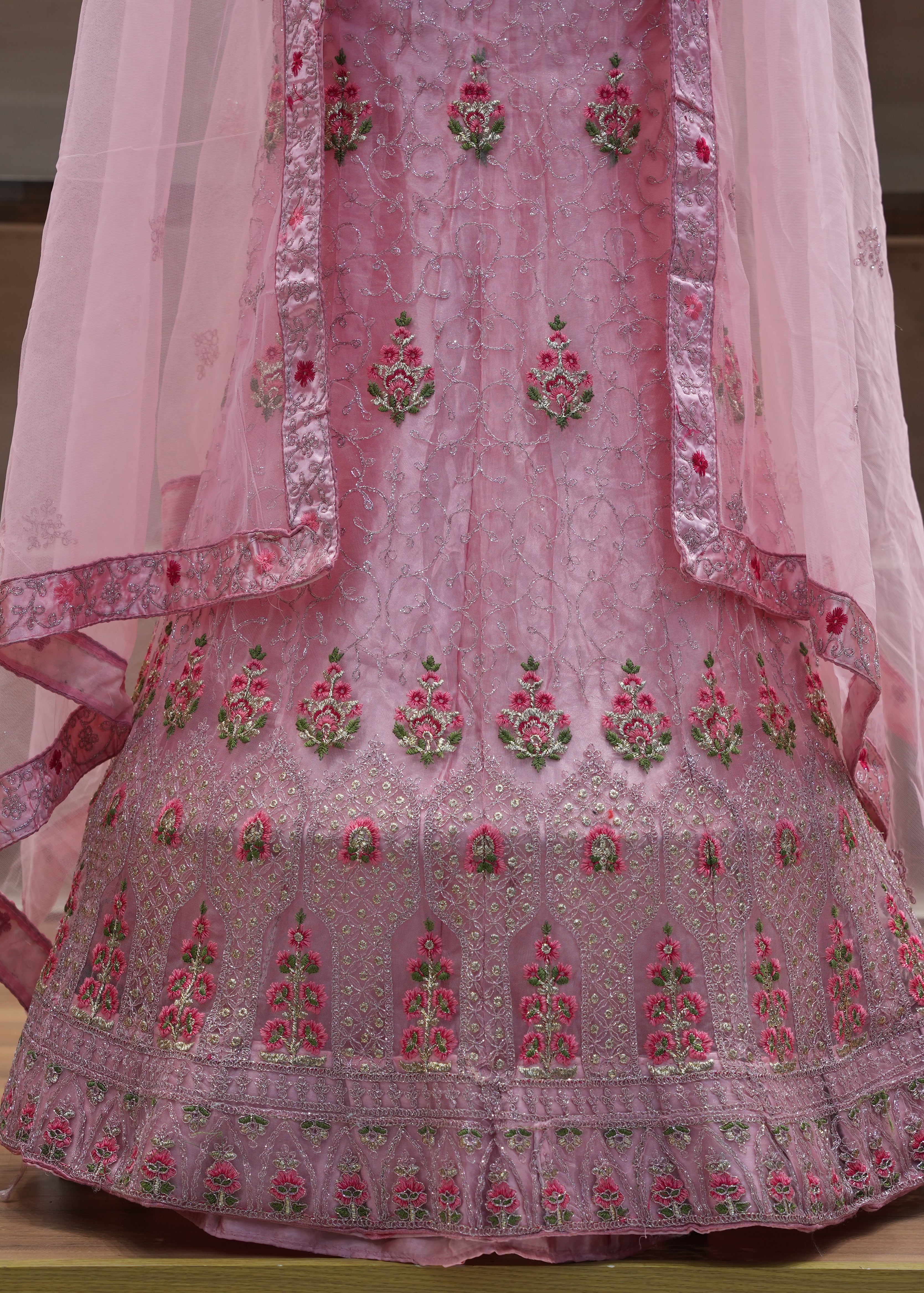 Pink embroidered traditional outfit with a sheer dupatta on a wooden surface.
