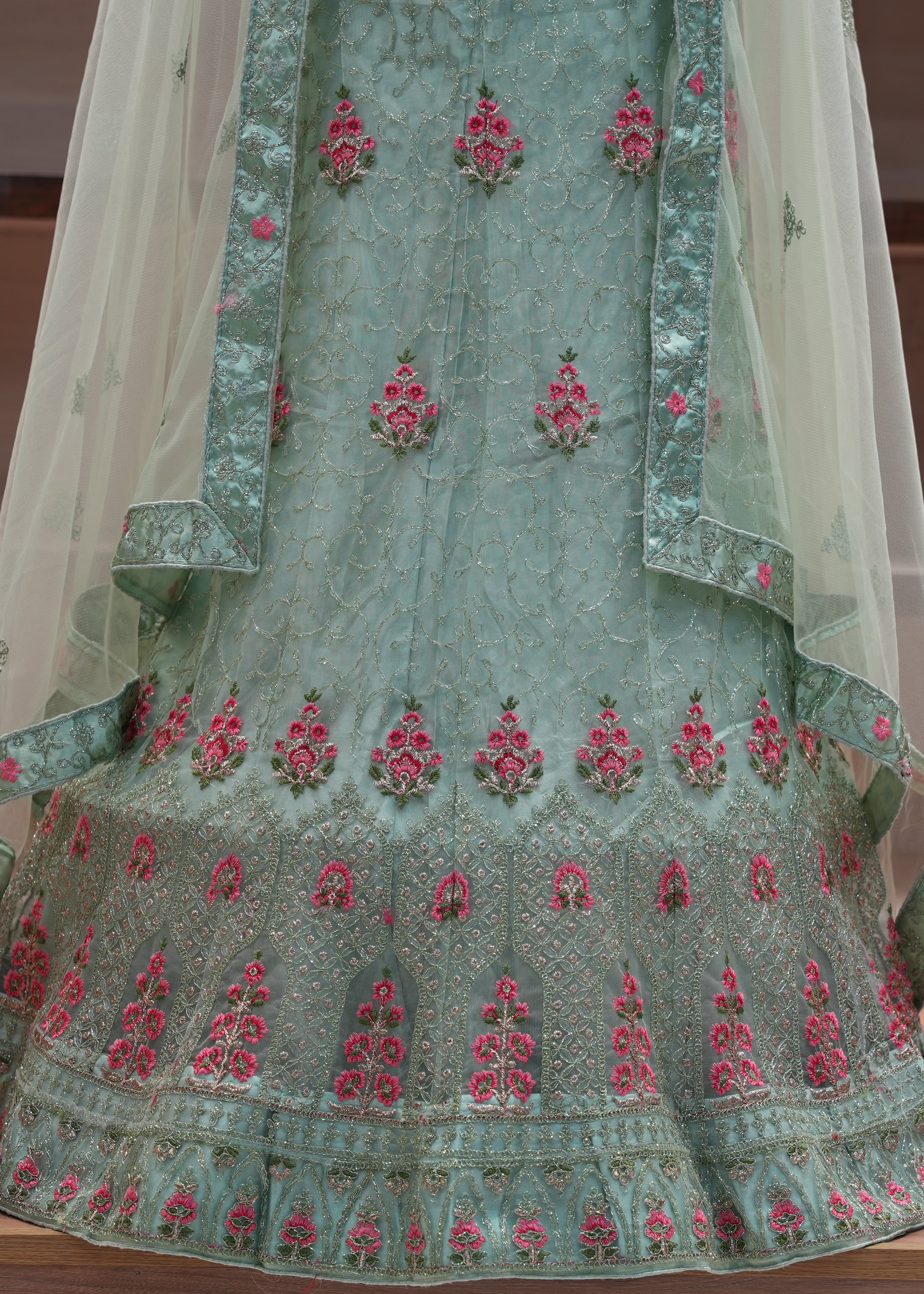 Green embroidered traditional outfit with pink floral patterns on a wooden surface.