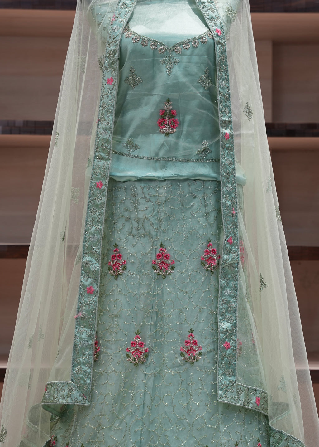 Traditional green embroidered outfit with a sheer dupatta on a wooden shelf background