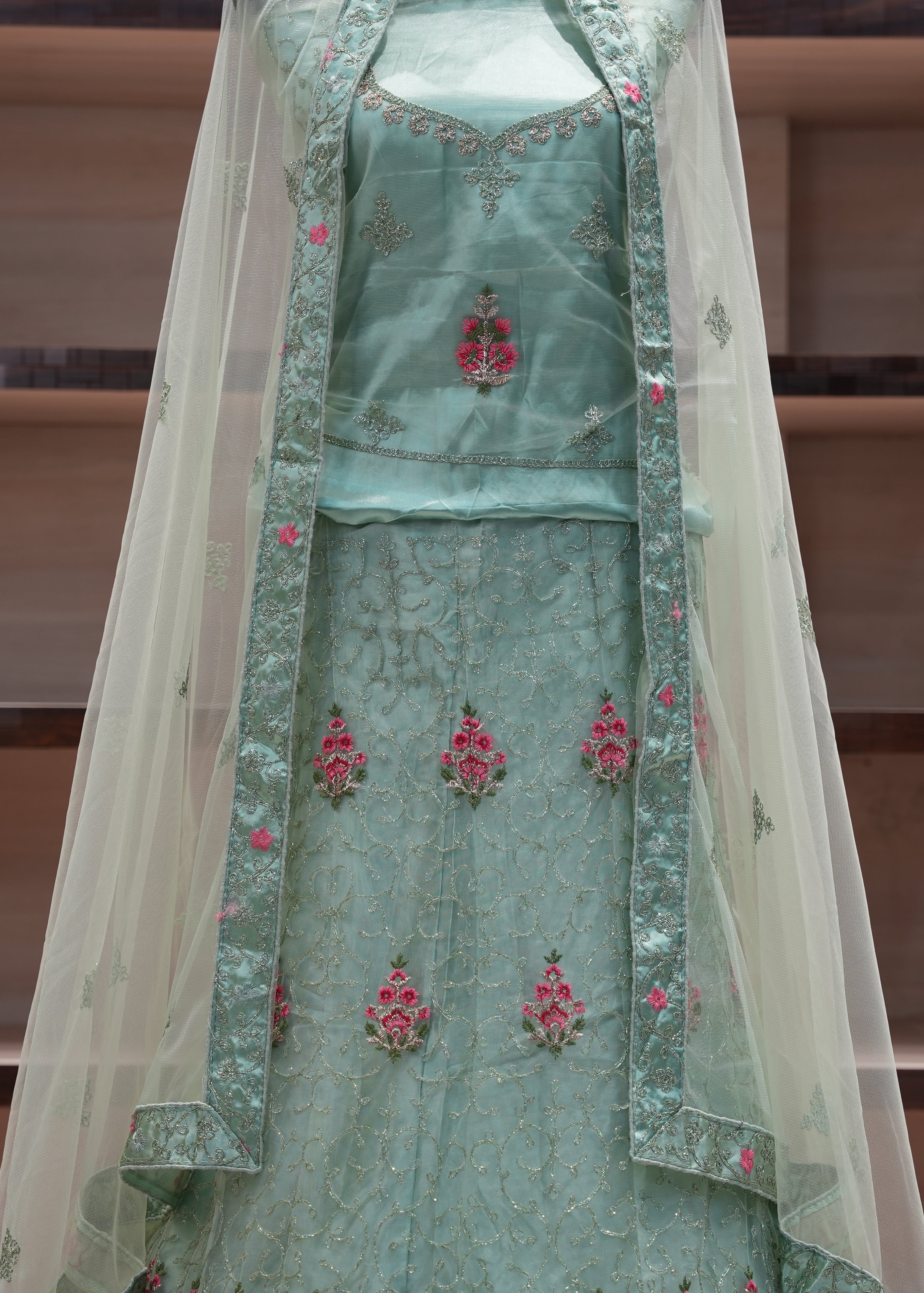 Traditional green embroidered outfit with a sheer dupatta on a wooden shelf background