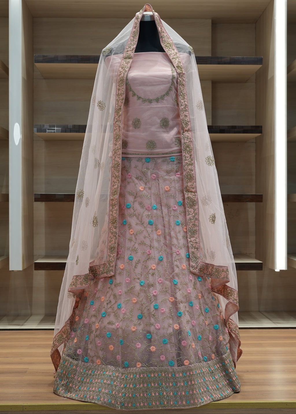 Pink embroidered traditional outfit with a sheer dupatta on a wooden shelf.