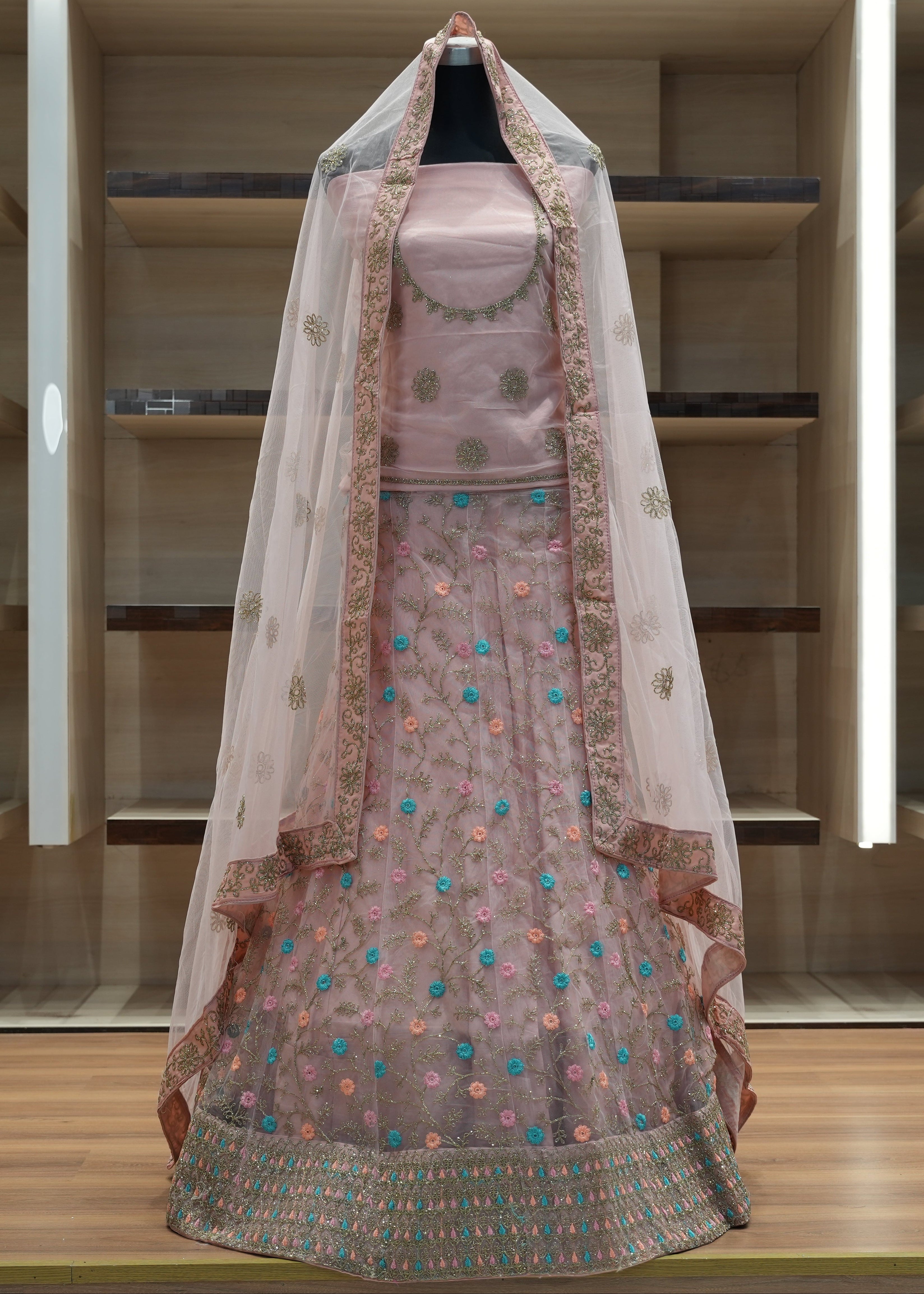 Pink embroidered traditional outfit with a sheer dupatta on a wooden shelf.
