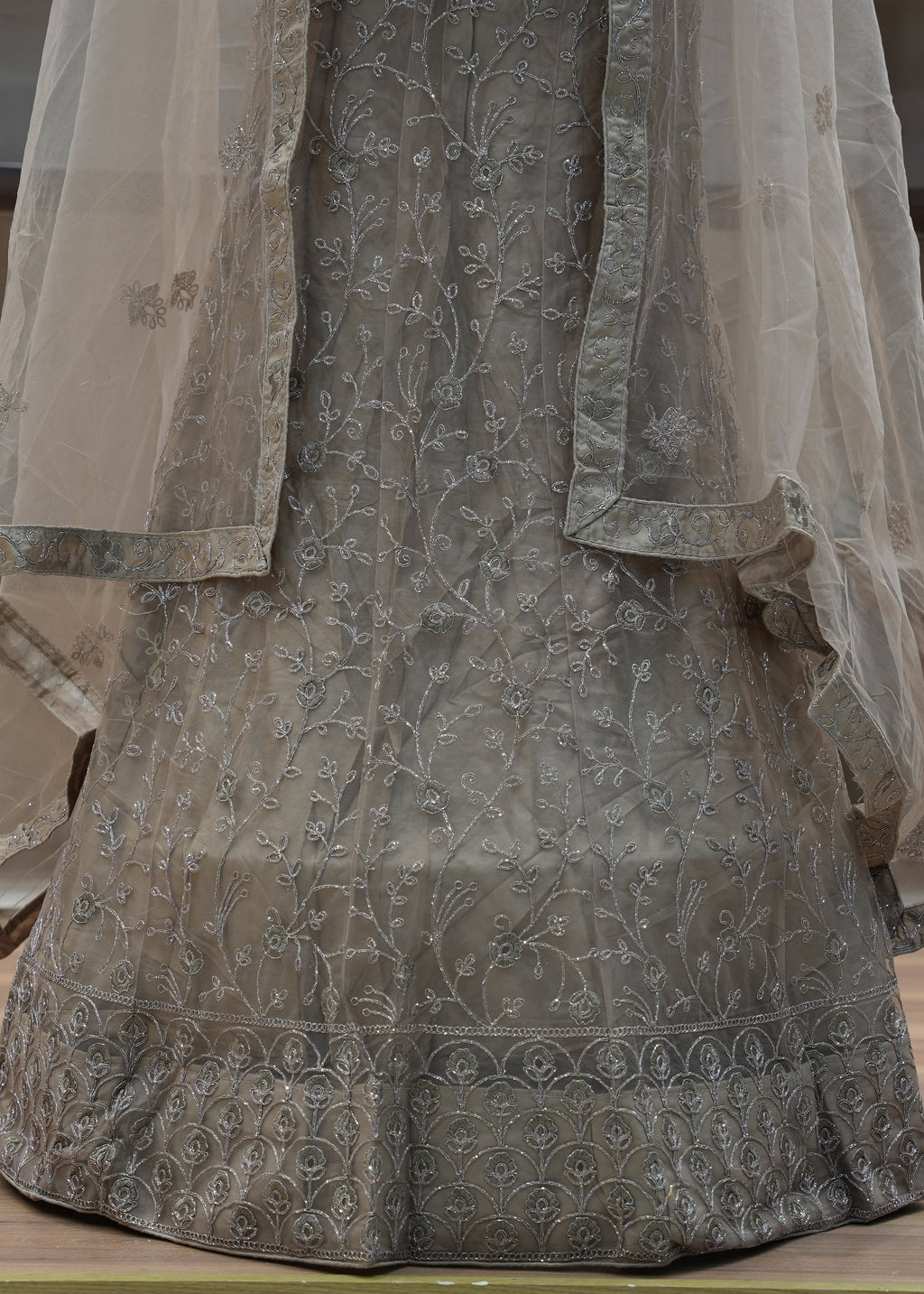 Traditional embroidered garment with a sheer overlay on a wooden surface