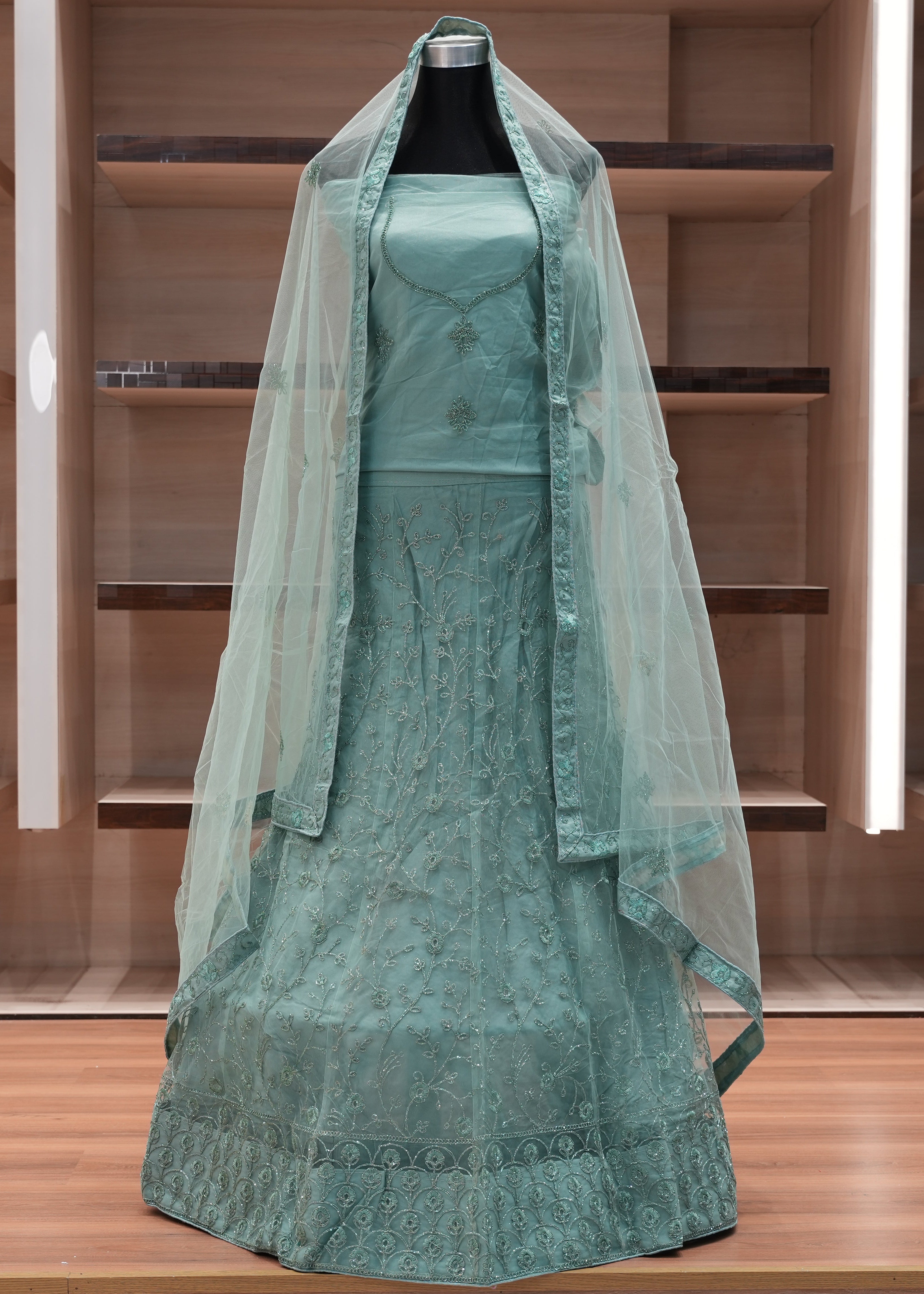 Teal embroidered dress with a sheer overlay on a mannequin against a wooden background