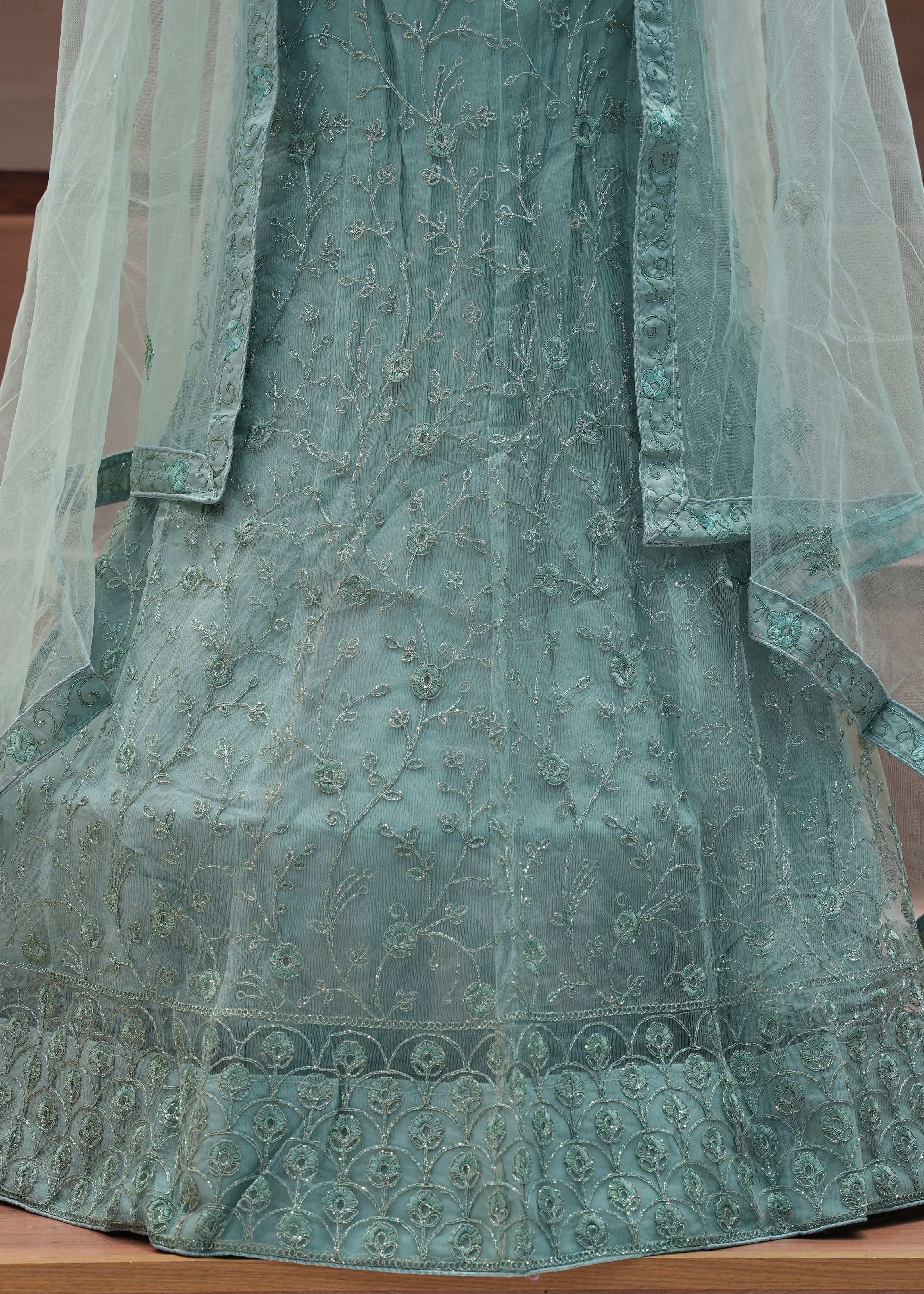 Green embroidered traditional outfit with a sheer overlay on a wooden surface