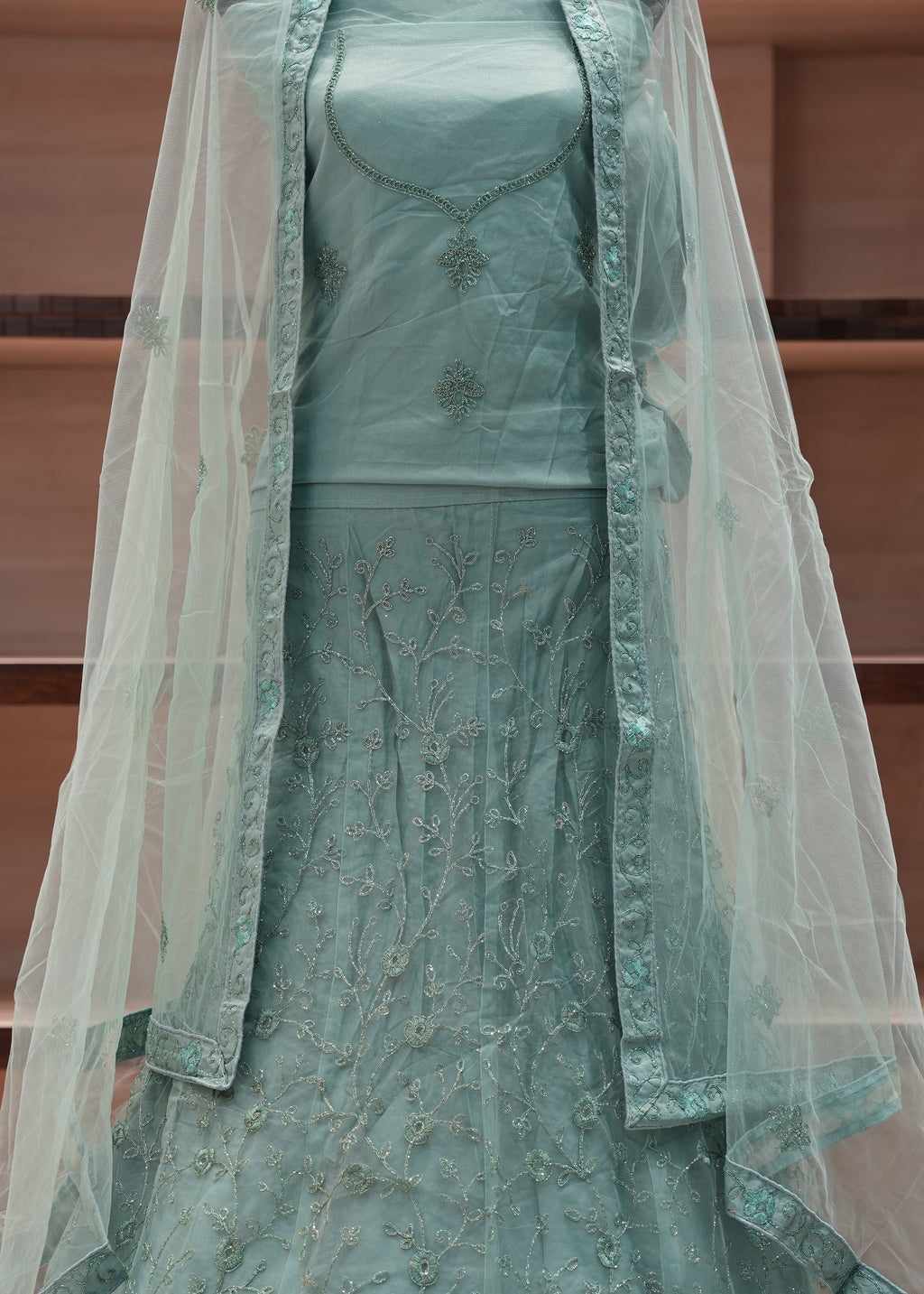 Teal embroidered dress with a sheer overlay against a wooden background