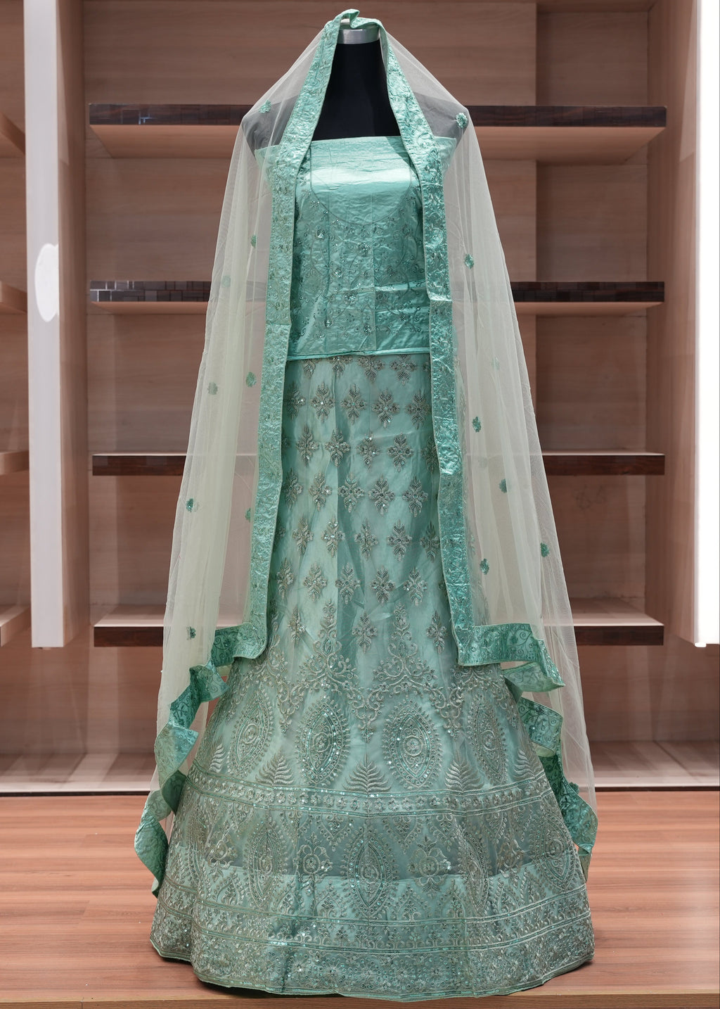 Green embroidered dress with a veil on a mannequin against a wooden background