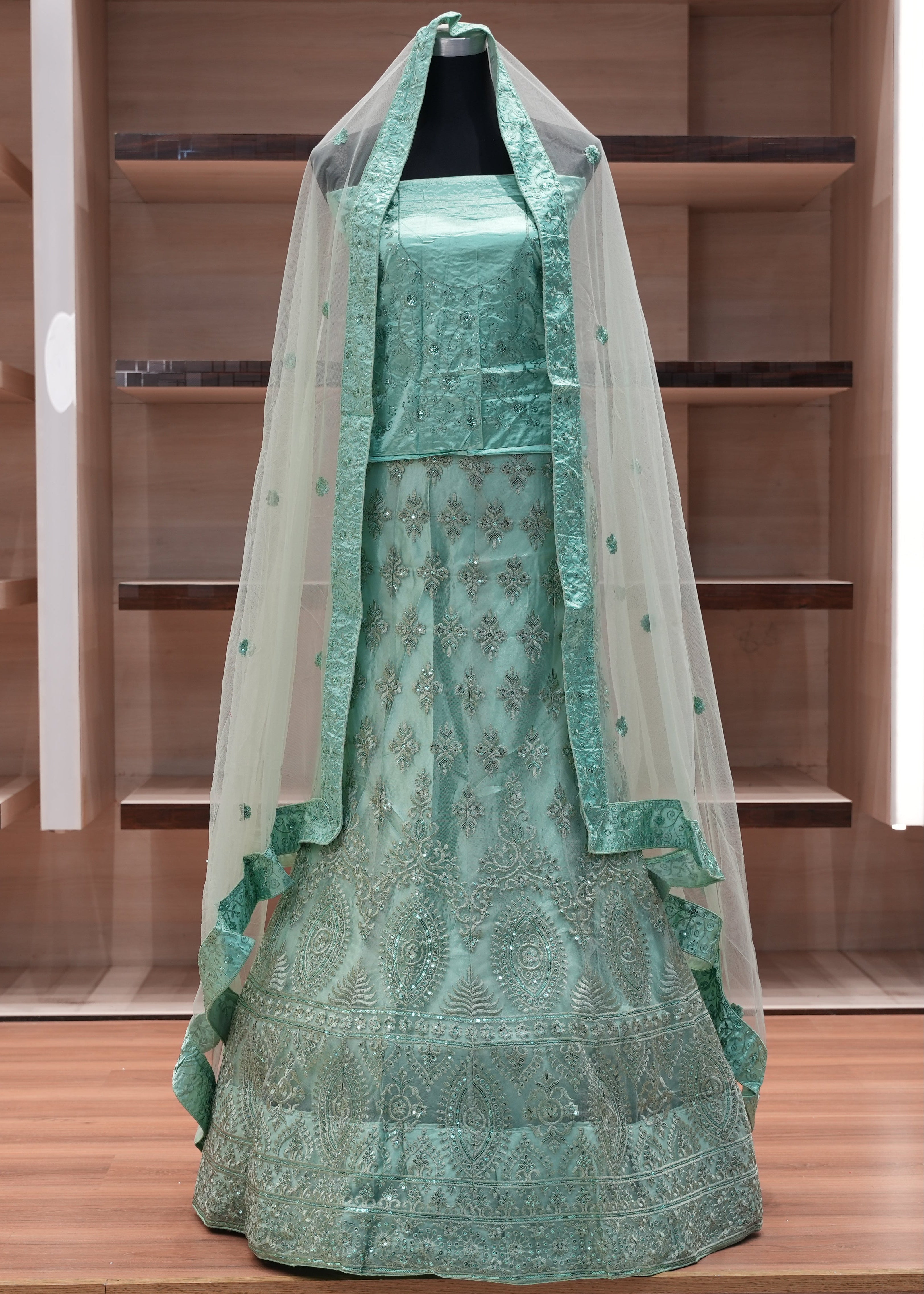 Green embroidered dress with a veil on a mannequin against a wooden background