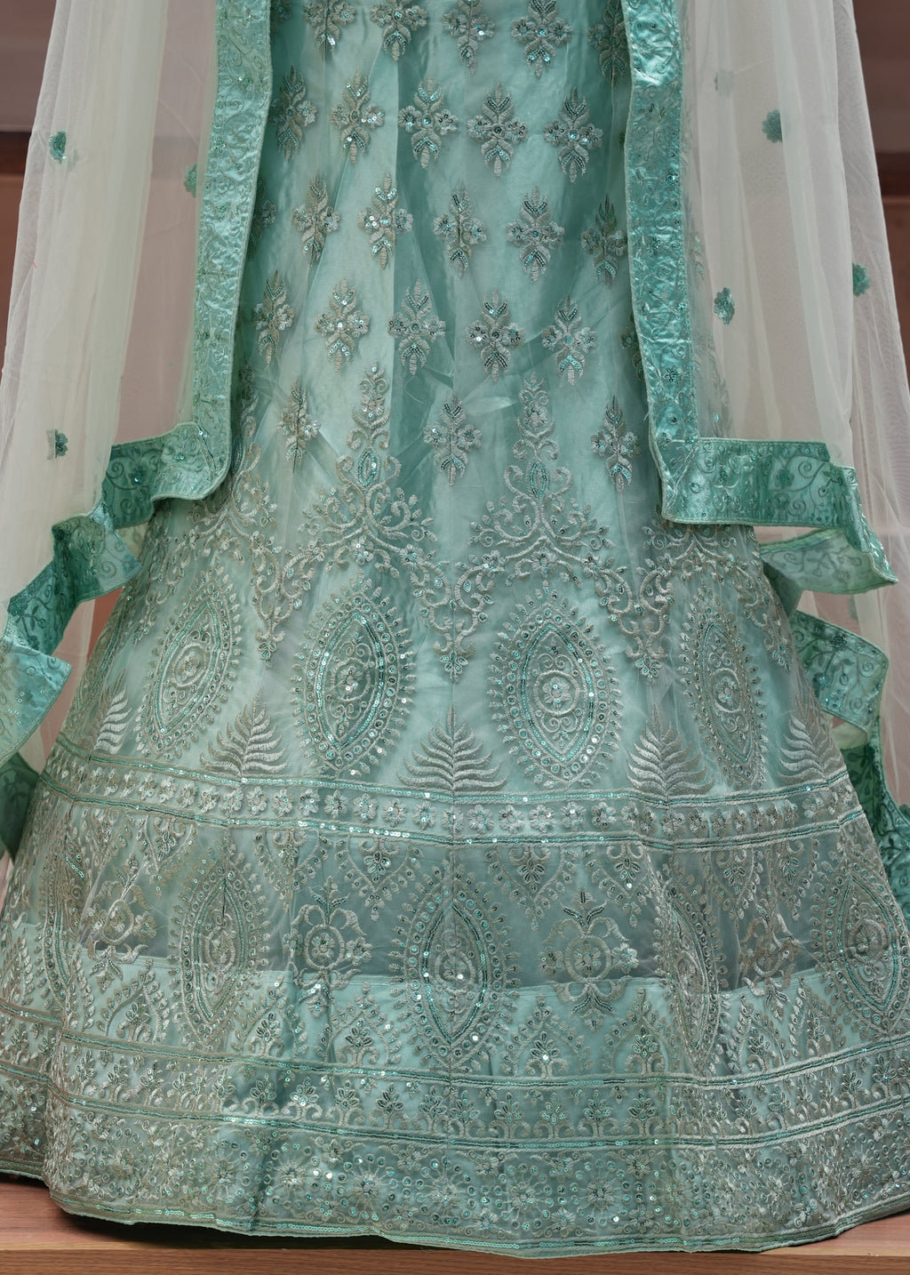 Green embroidered traditional outfit with a sheer dupatta on a wooden surface