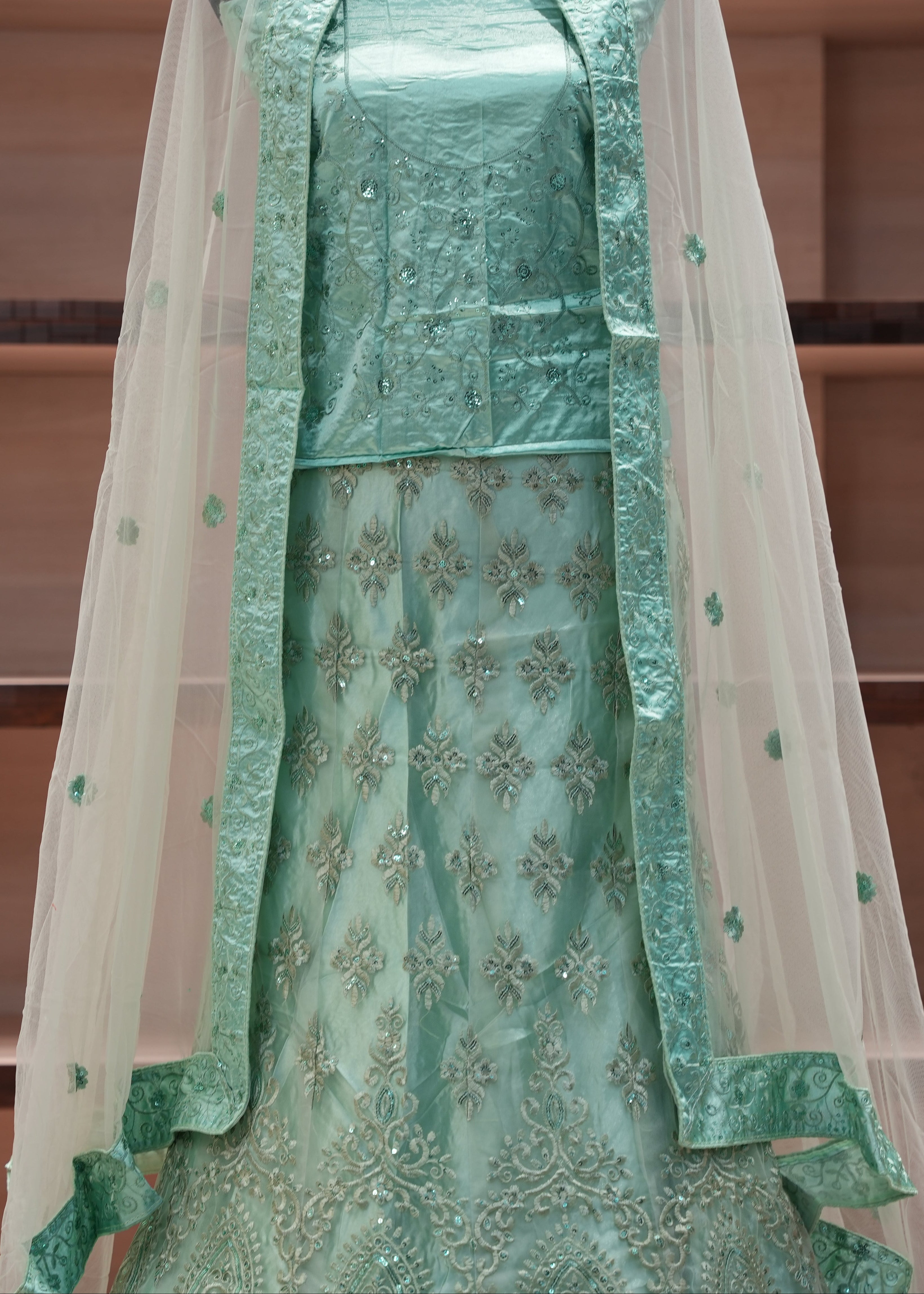 Green embroidered traditional outfit with a sheer dupatta on a wooden shelf background