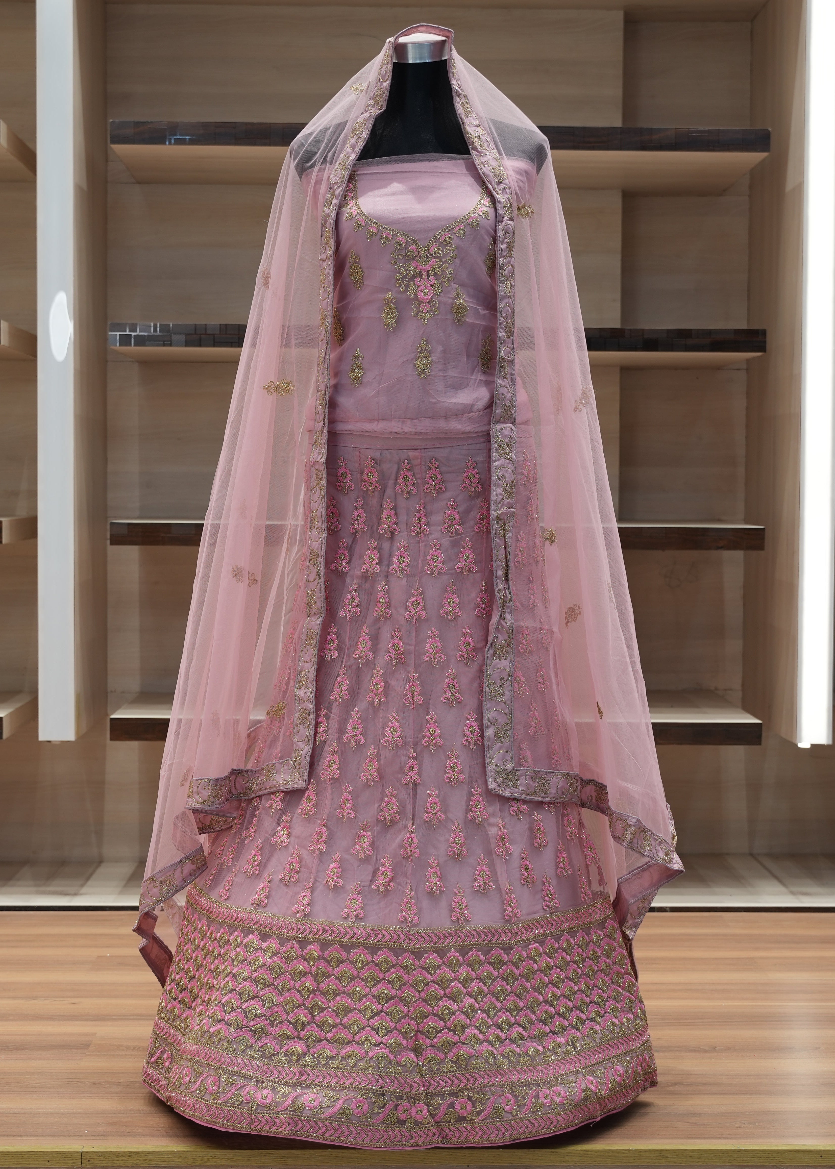 Pink embroidered traditional outfit with a veil on a mannequin against a wooden background