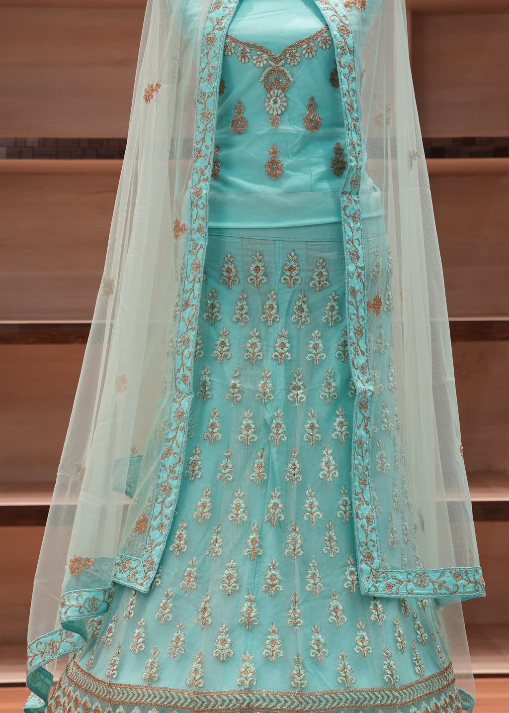 Turquoise embroidered traditional outfit with a sheer dupatta on a wooden background
