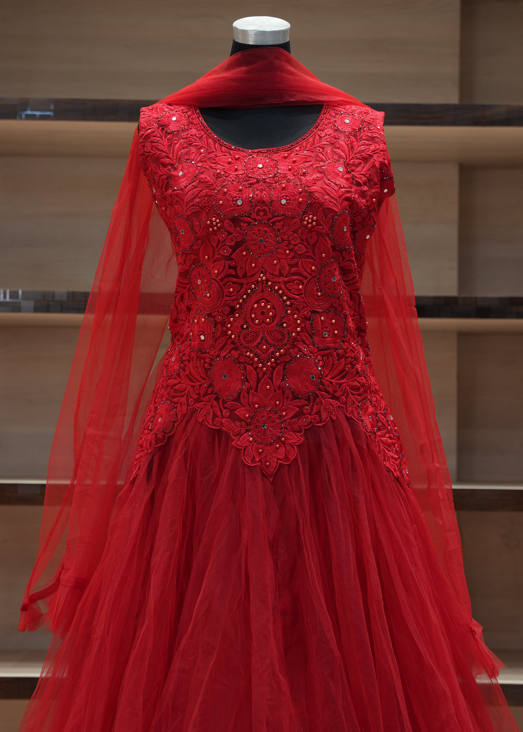 Red embroidered dress on a mannequin against a wooden shelf background