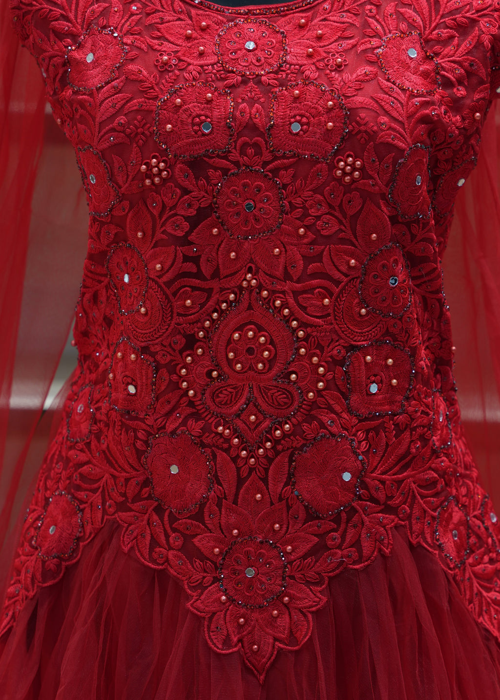 Close-up of a red embroidered fabric with intricate patterns and embellishments.