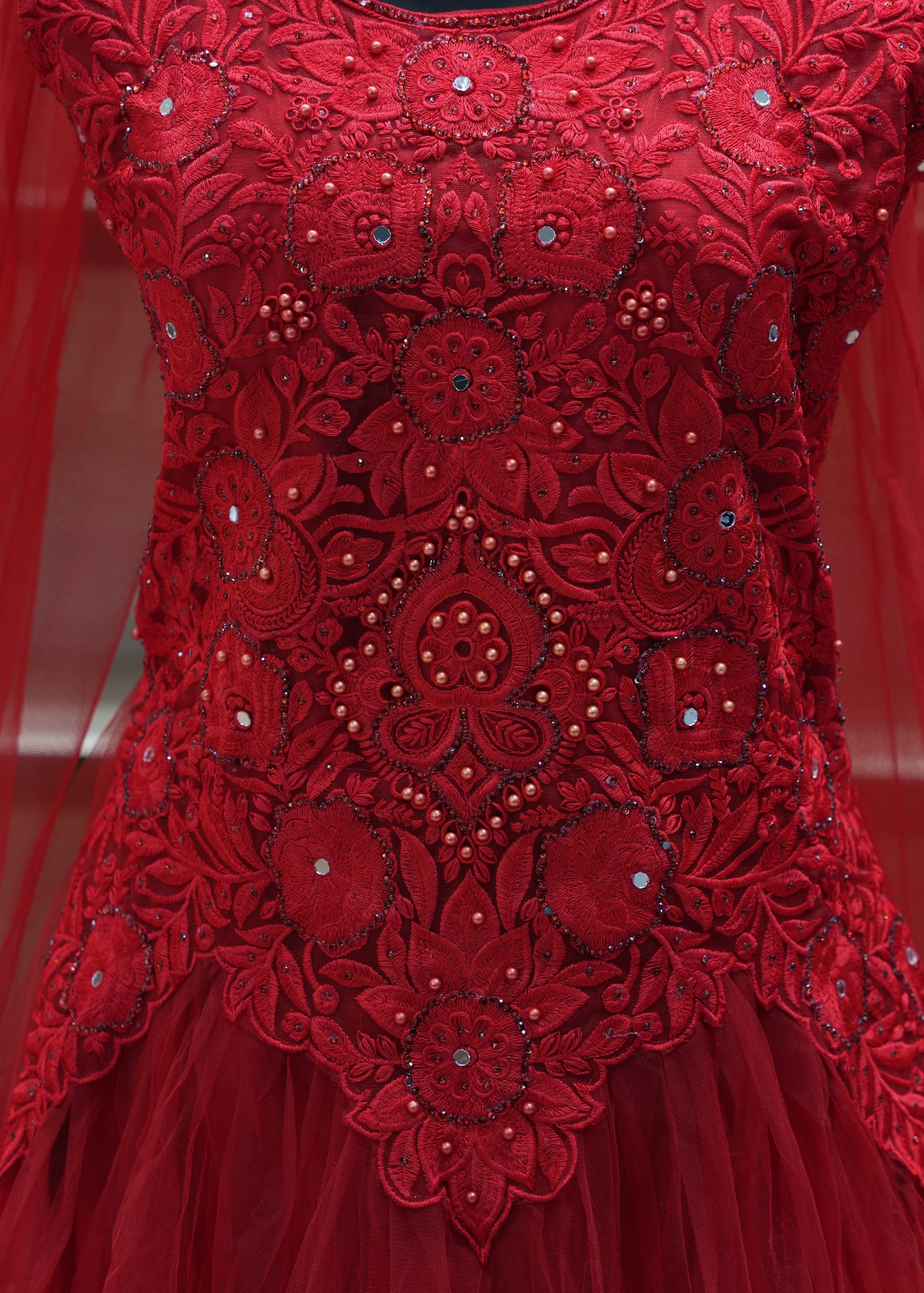 Close-up of a red embroidered fabric with intricate patterns and embellishments.