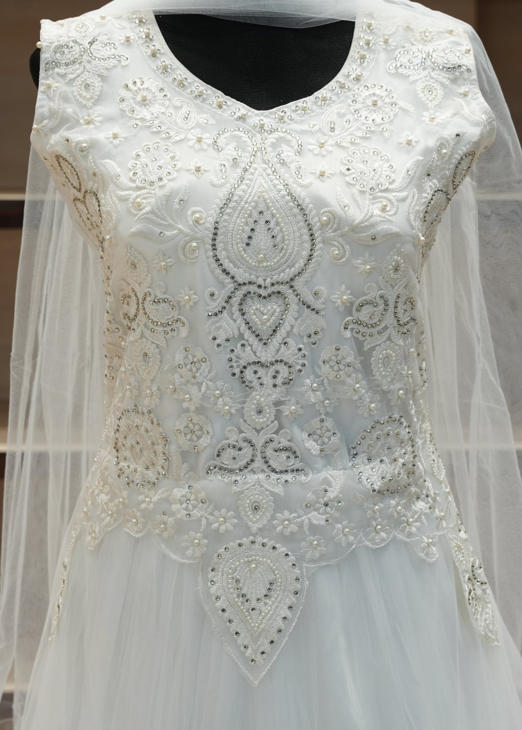 White embroidered dress with a sheer overlay on a wooden shelf background