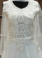 White embroidered dress with a sheer overlay on a wooden shelf background